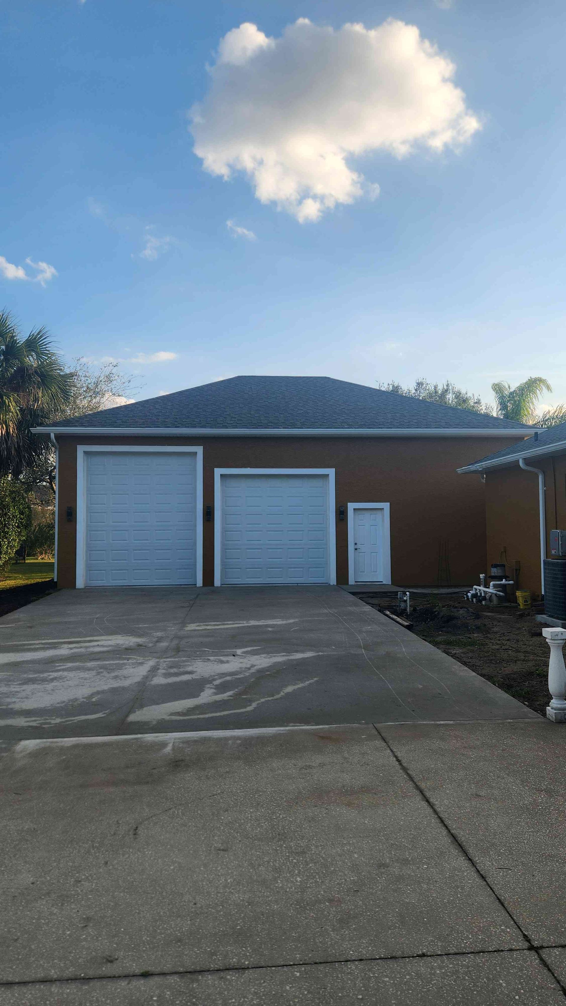 Two-car garage with white doors and a concrete driveway under a blue sky with a small cloud