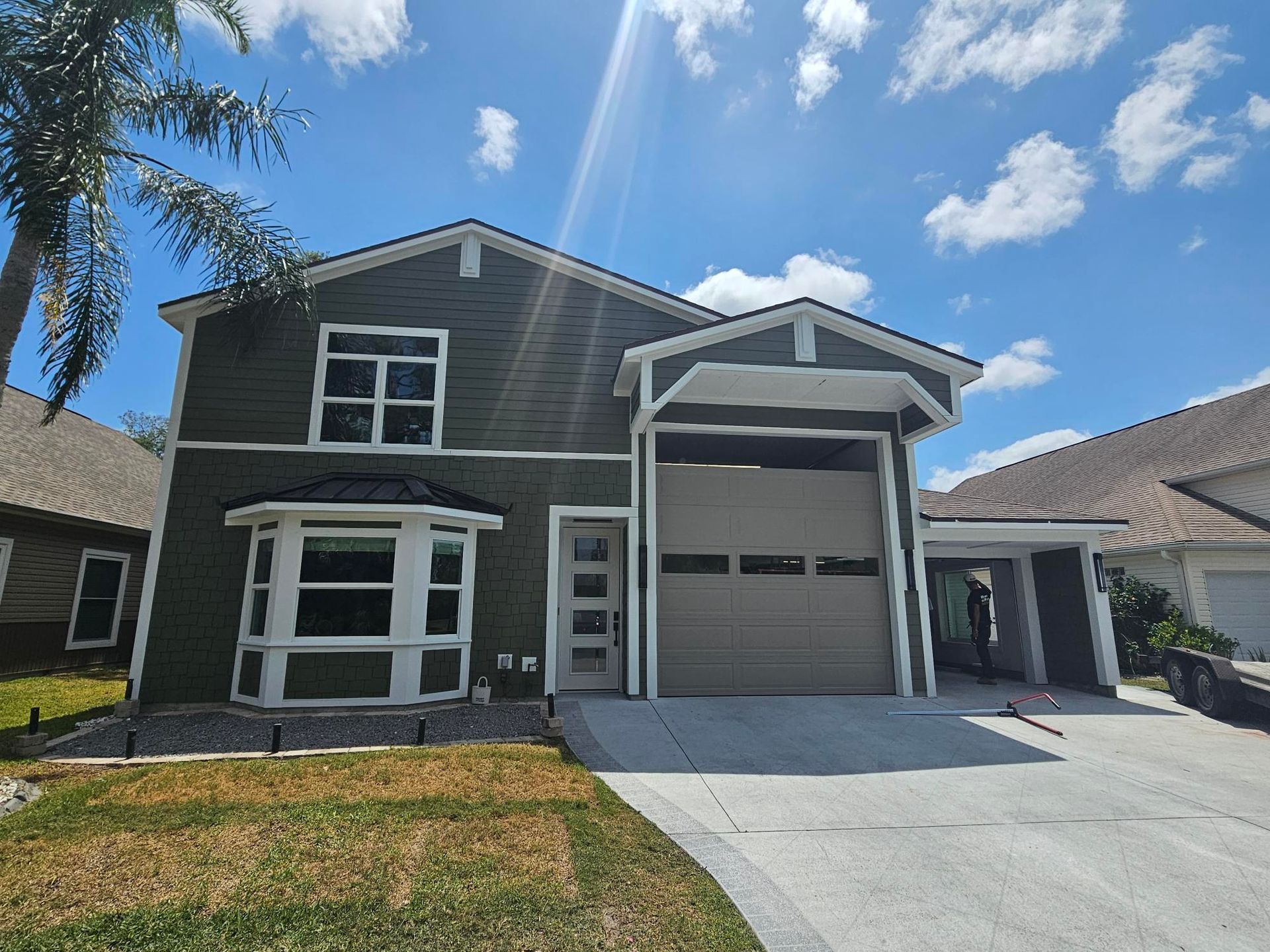 Two-story gray house with white trim, a garage, and a concrete driveway under a blue sky