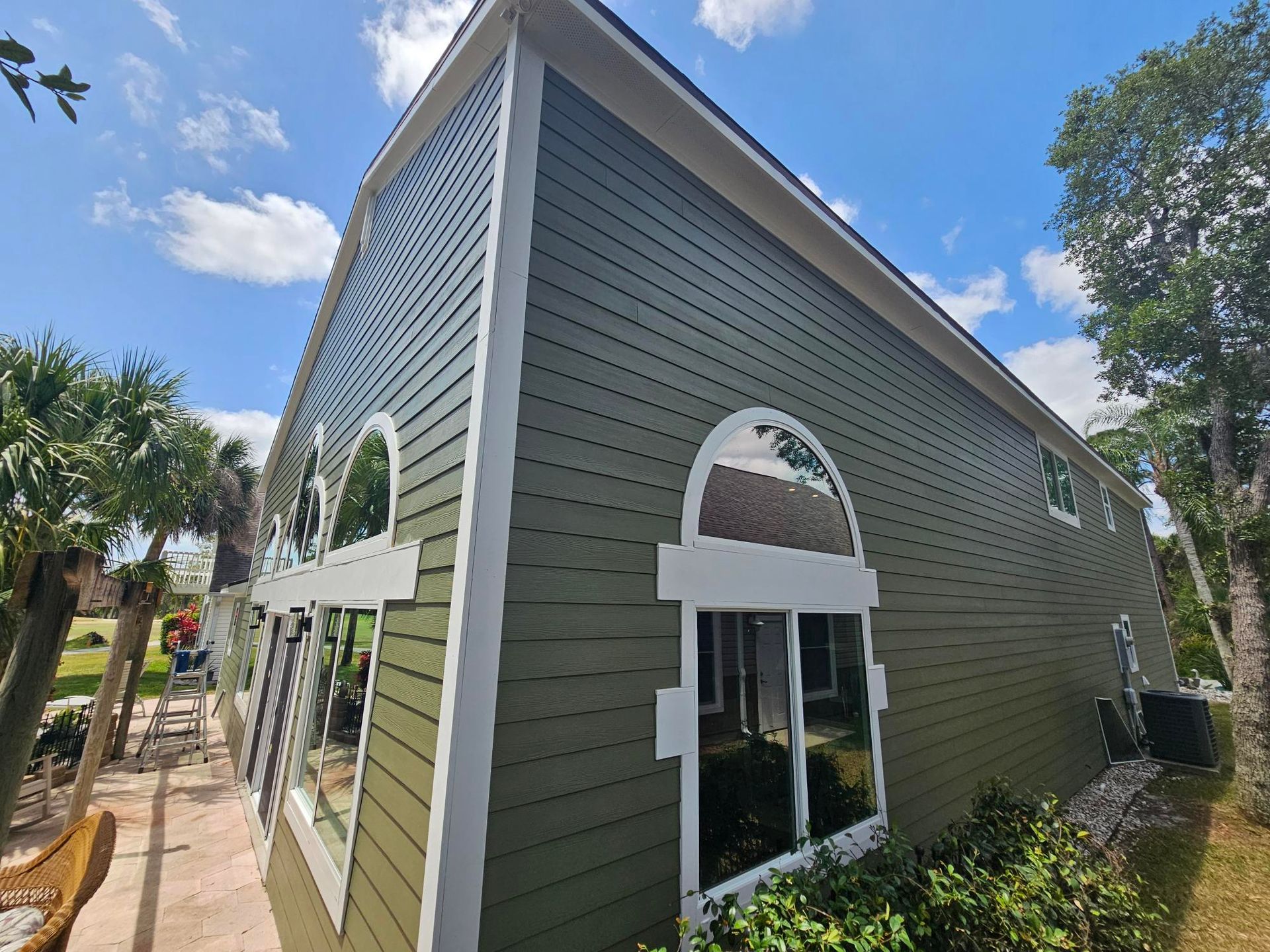 Green house exterior with white trim and arched windows under a blue sky