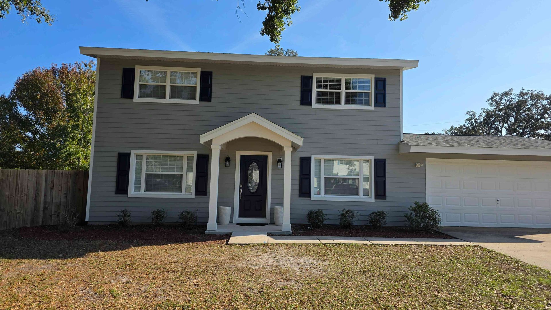 Two-story gray house with white trim, front porch, and attached garage under a clear blue sky