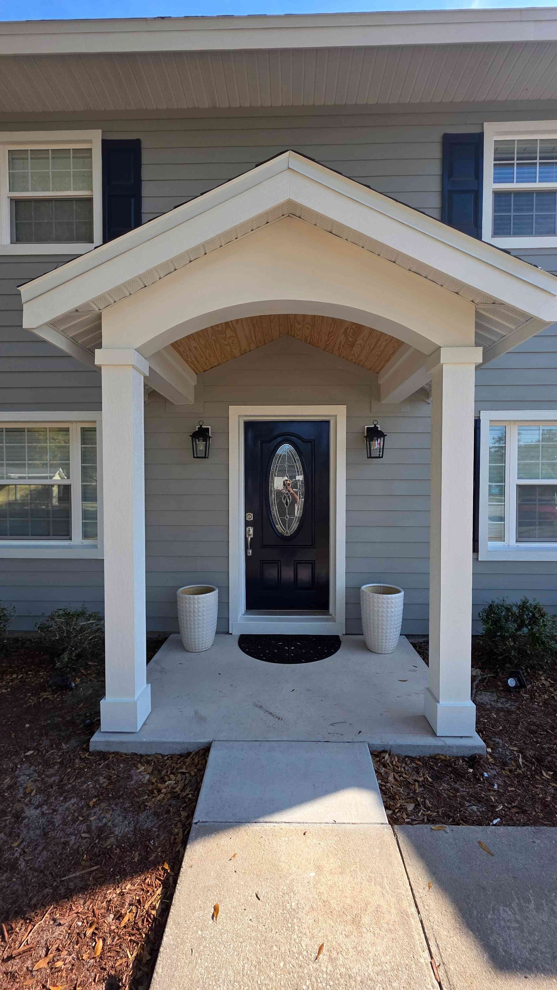 Front porch entrance to a house with a small covered entry, white columns, and a black front door