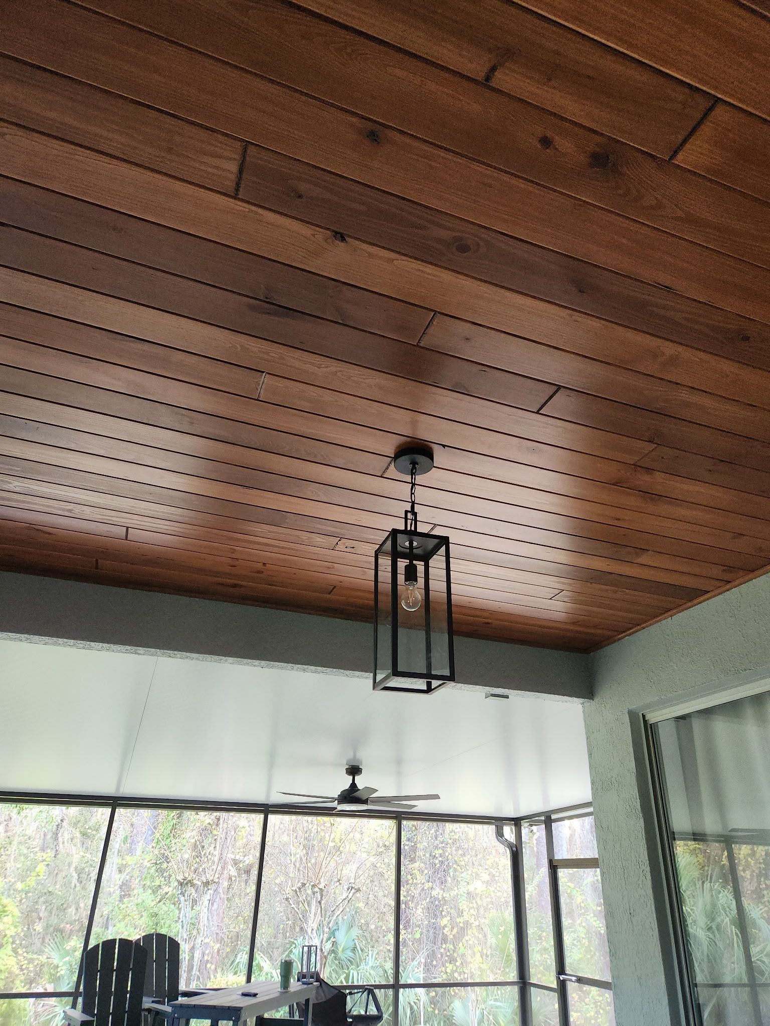 Wood-paneled porch ceiling with a hanging lantern over screened windows and outdoor trees.