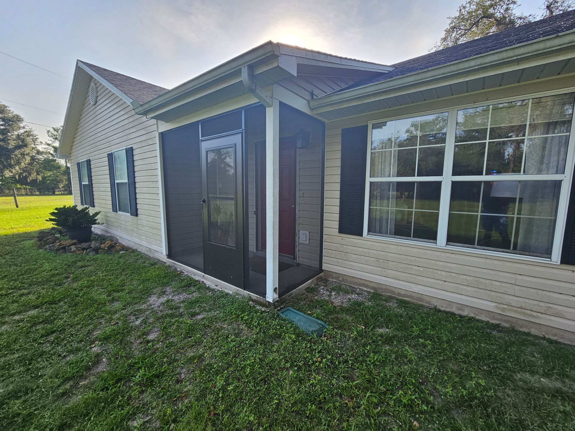 Side view of a beige house with a screened porch, white trim, and green lawn in front
