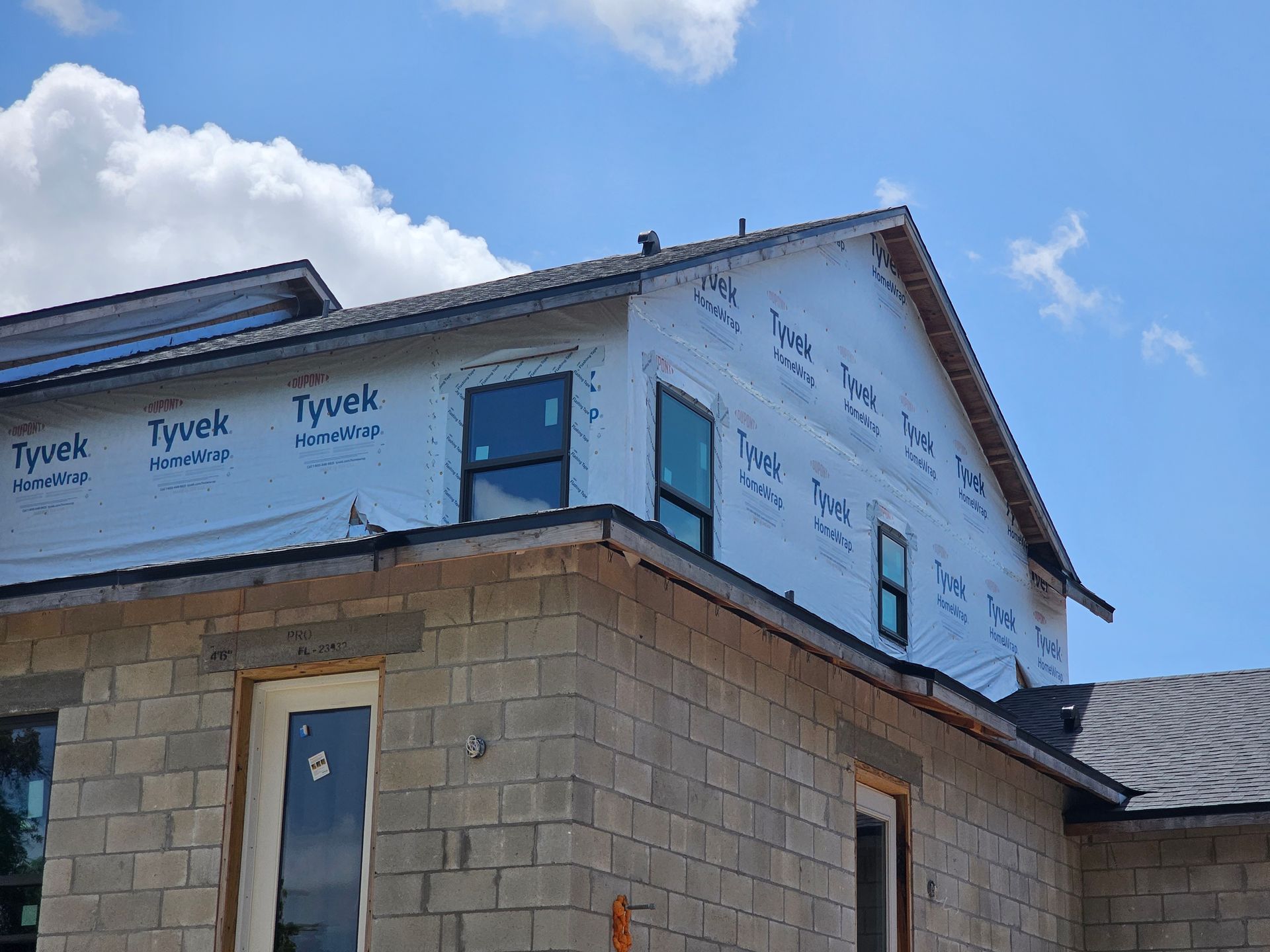 Partially built house with stone walls and white house wrap under a blue sky