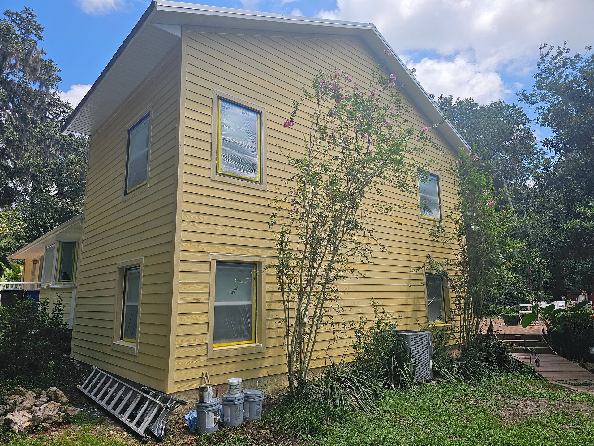 Yellow two-story house with white trim, surrounded by trees and greenery