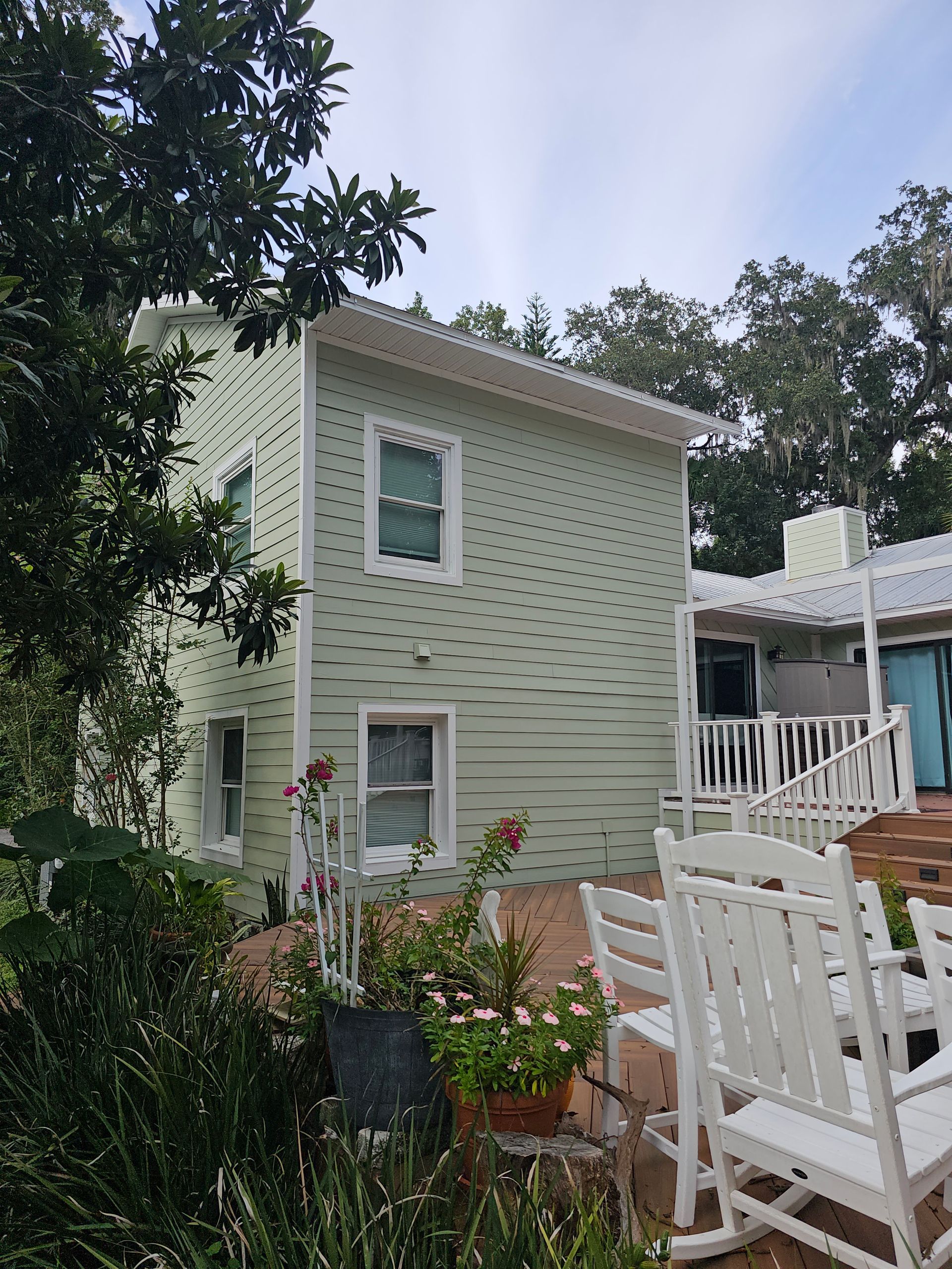 Backyard patio beside a pale green house with white porch railing and a striped canopy