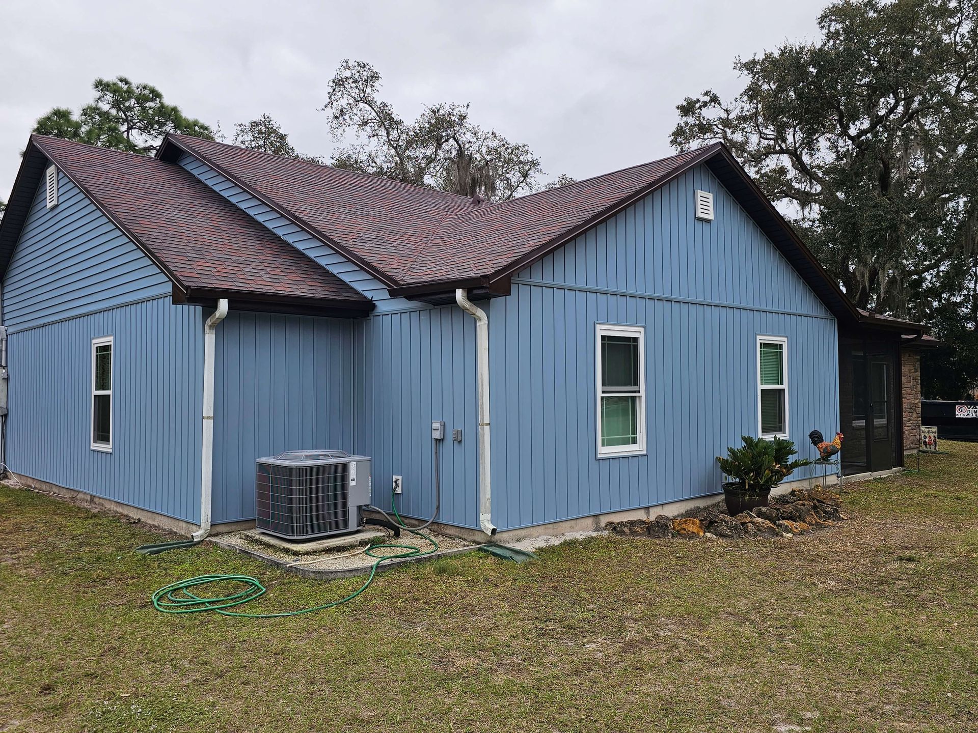 Blue house with a maroon roof and white-trimmed windows on a grassy lot under cloudy skies