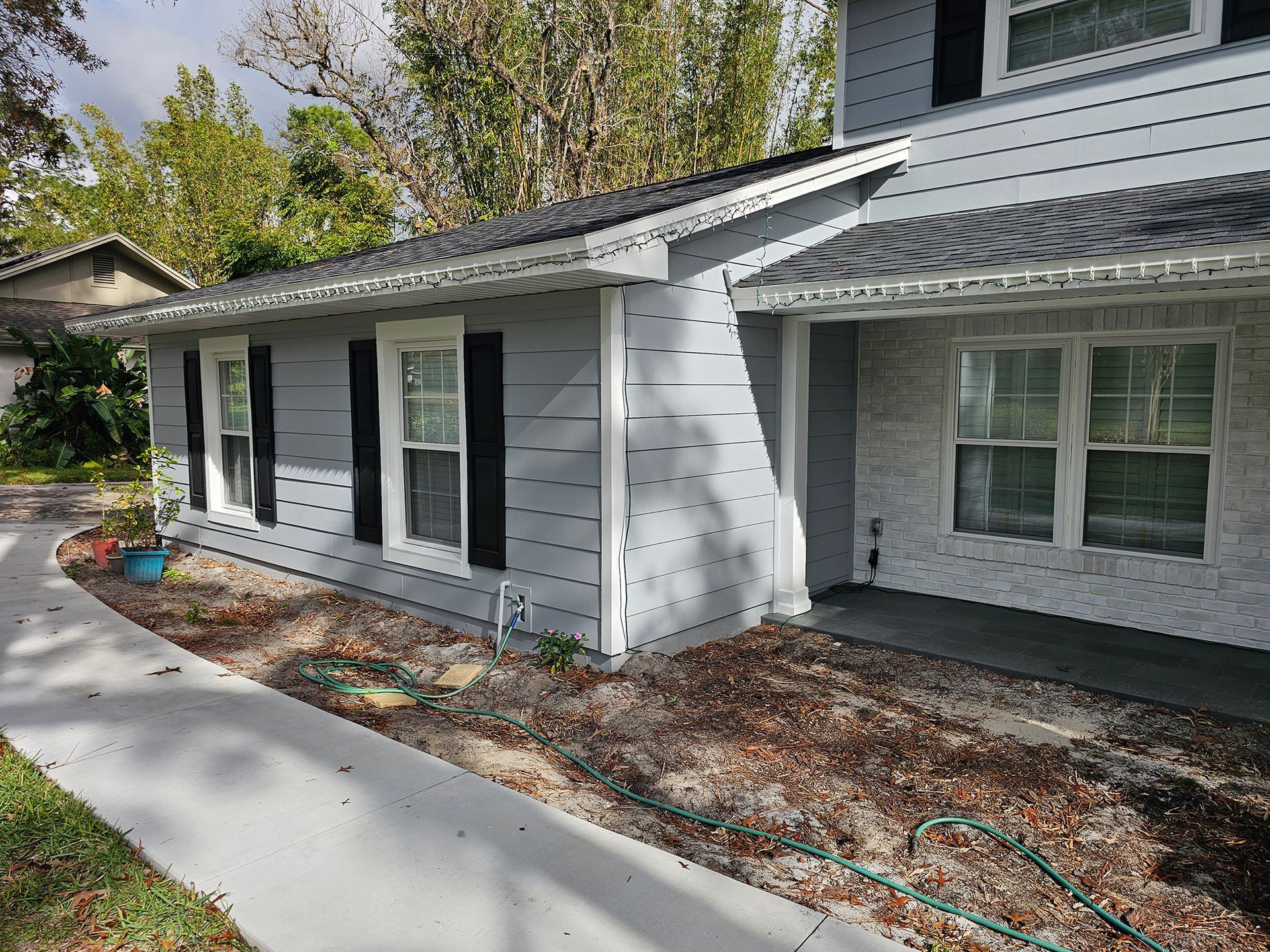 Front of a gray house with white trim, black shutters, a concrete walkway, and flower bed landscaping.