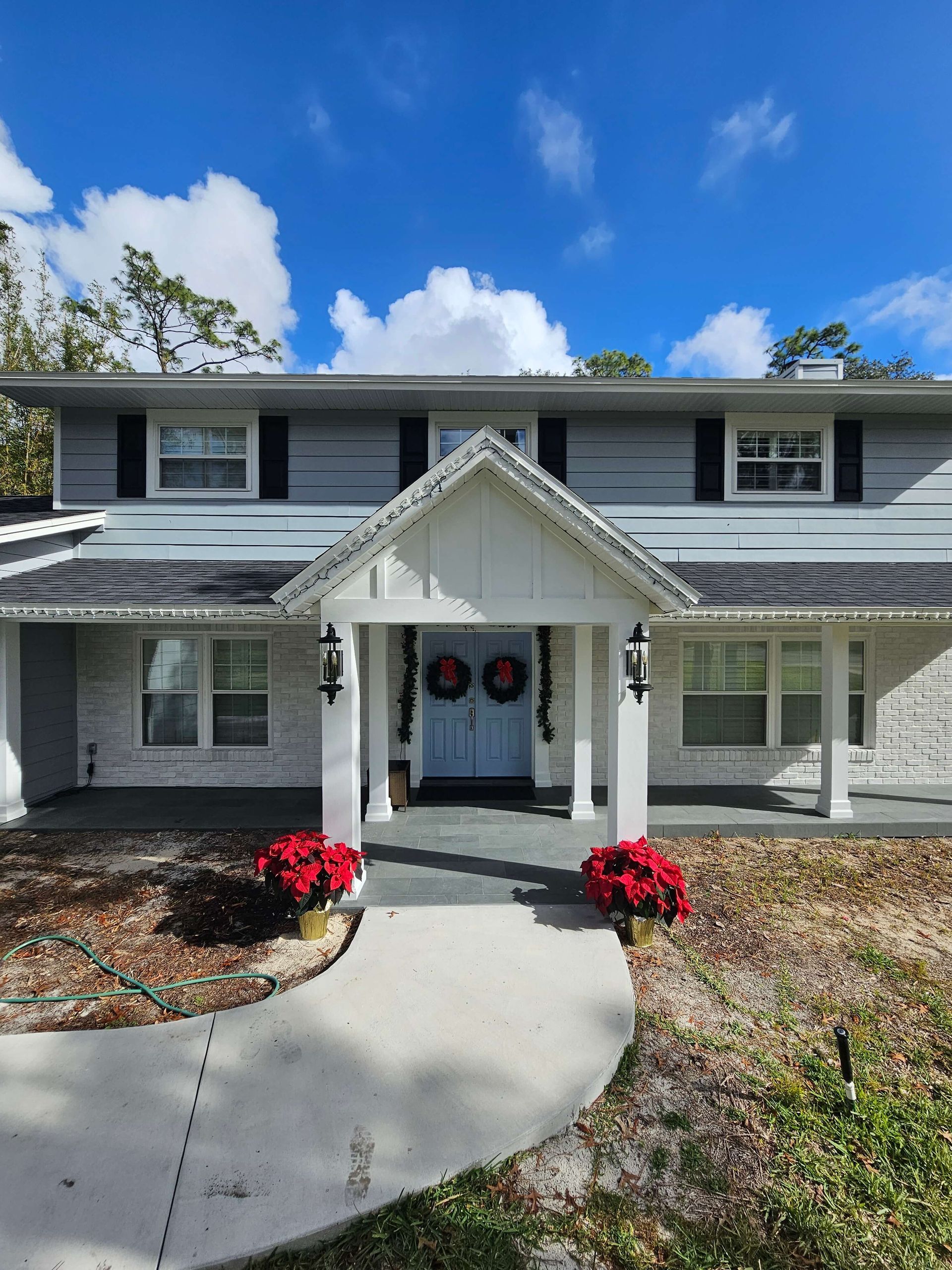 Two-story gray house with white trim, front porch, and red flower planters under a blue sky.