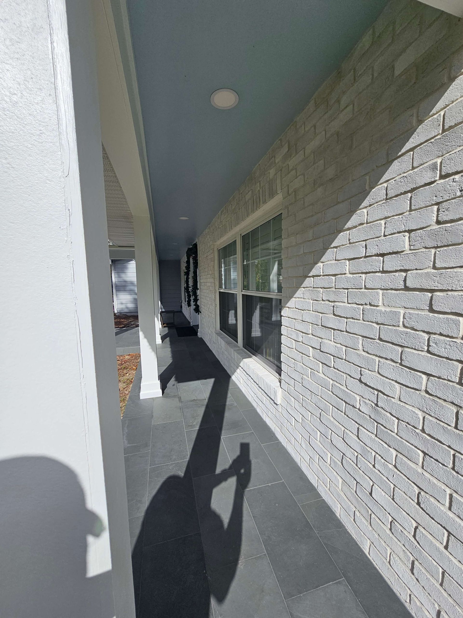 Covered sidewalk beside white brick building, with windows, pillars, and long shadows in bright daylight.