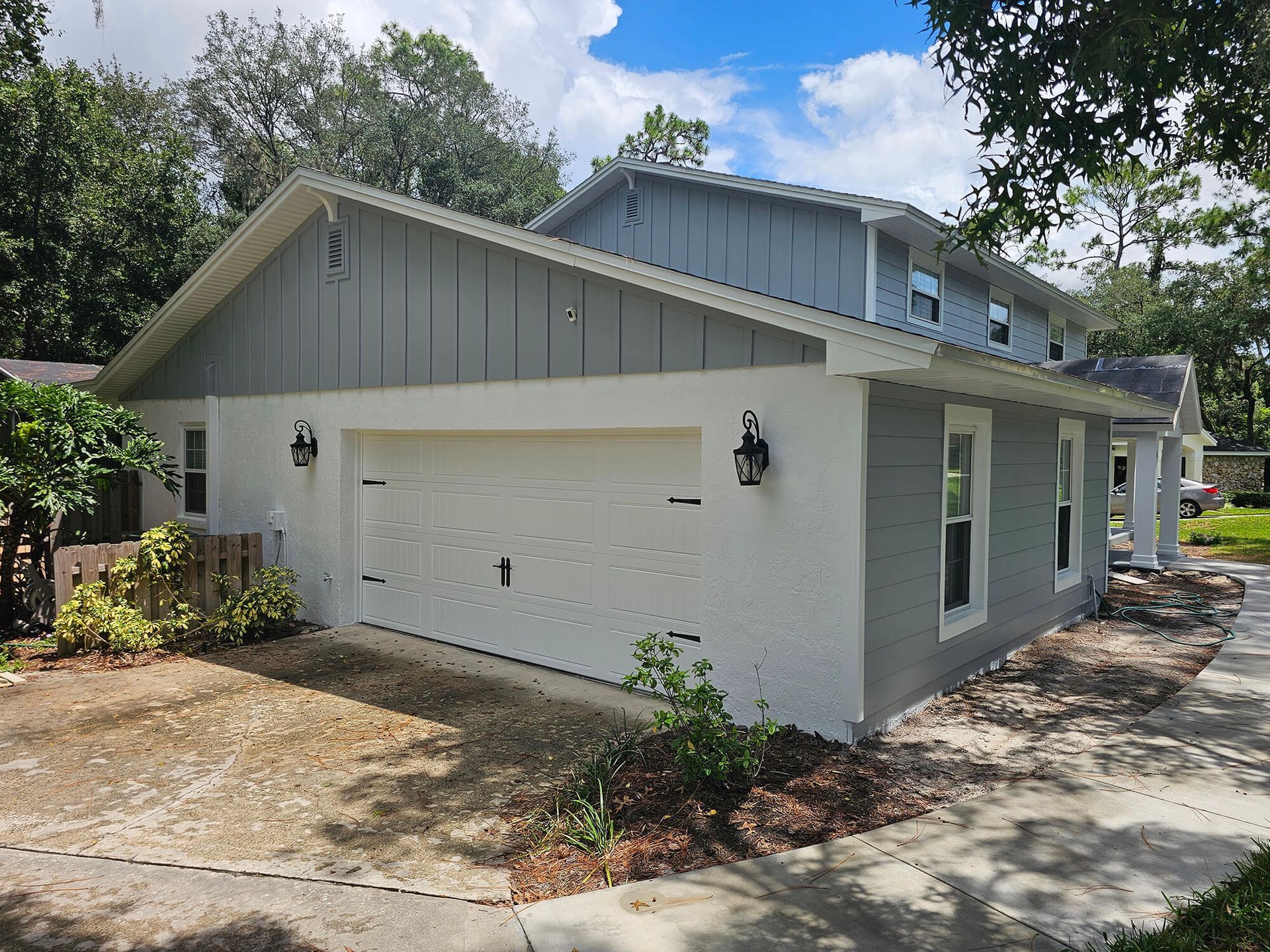 White single-story house with attached garage, gray roof, and front walkway in a sunny yard