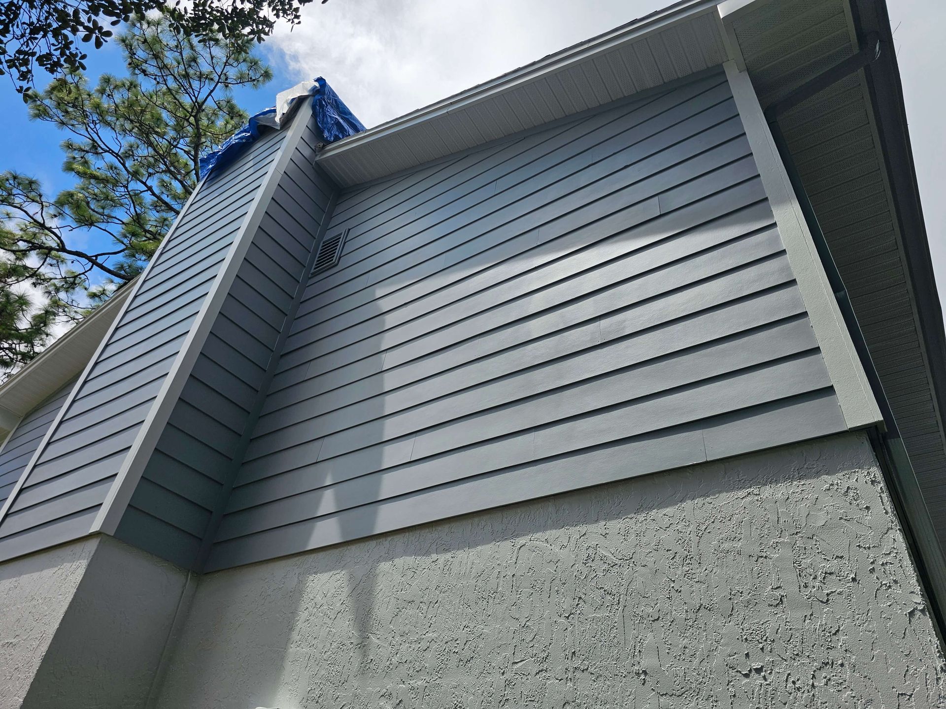 Gray house exterior with blue siding and sloped roof against a partly cloudy sky