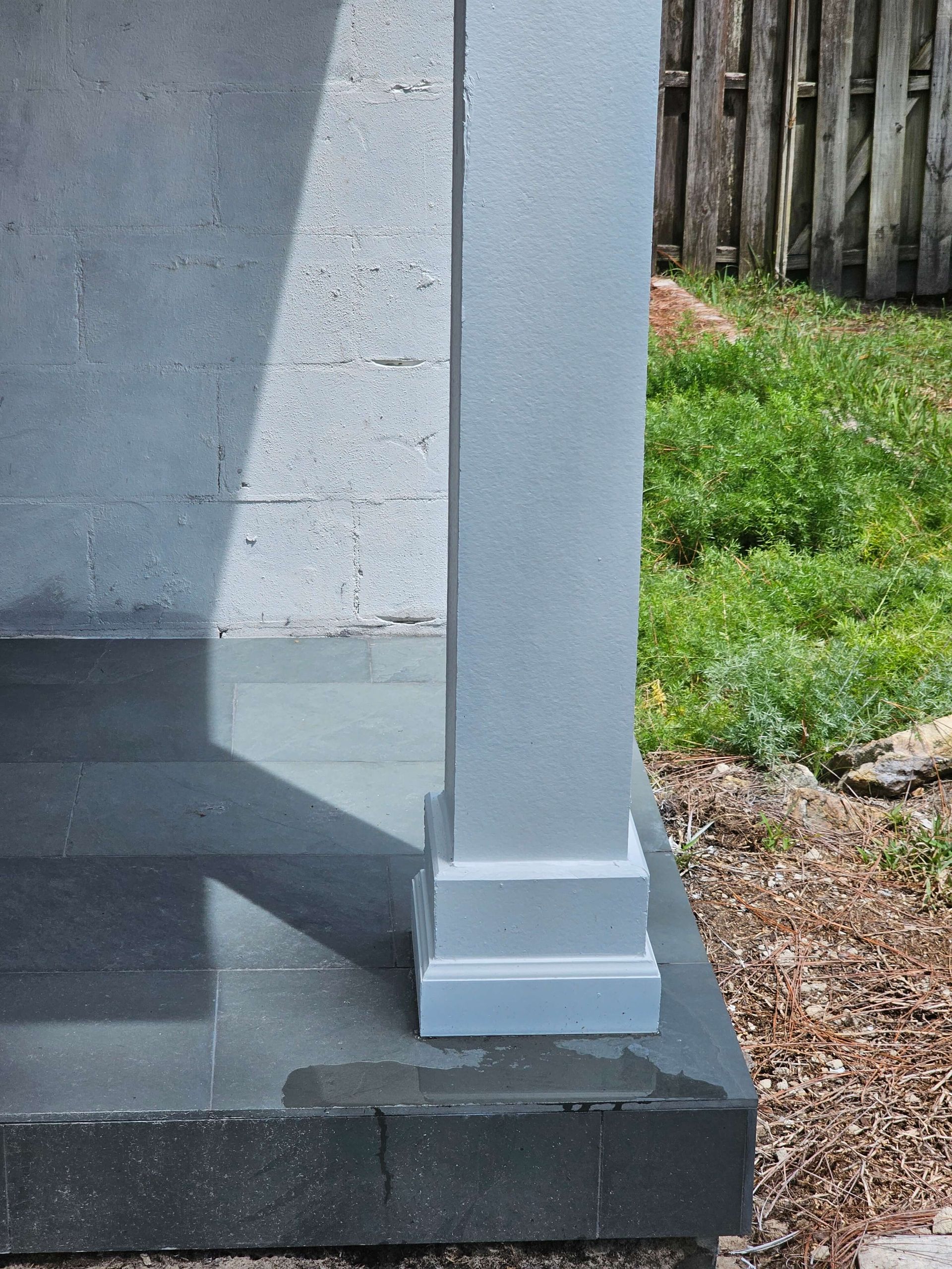White porch post on dark gray concrete steps beside a grassy yard and wooden fence.