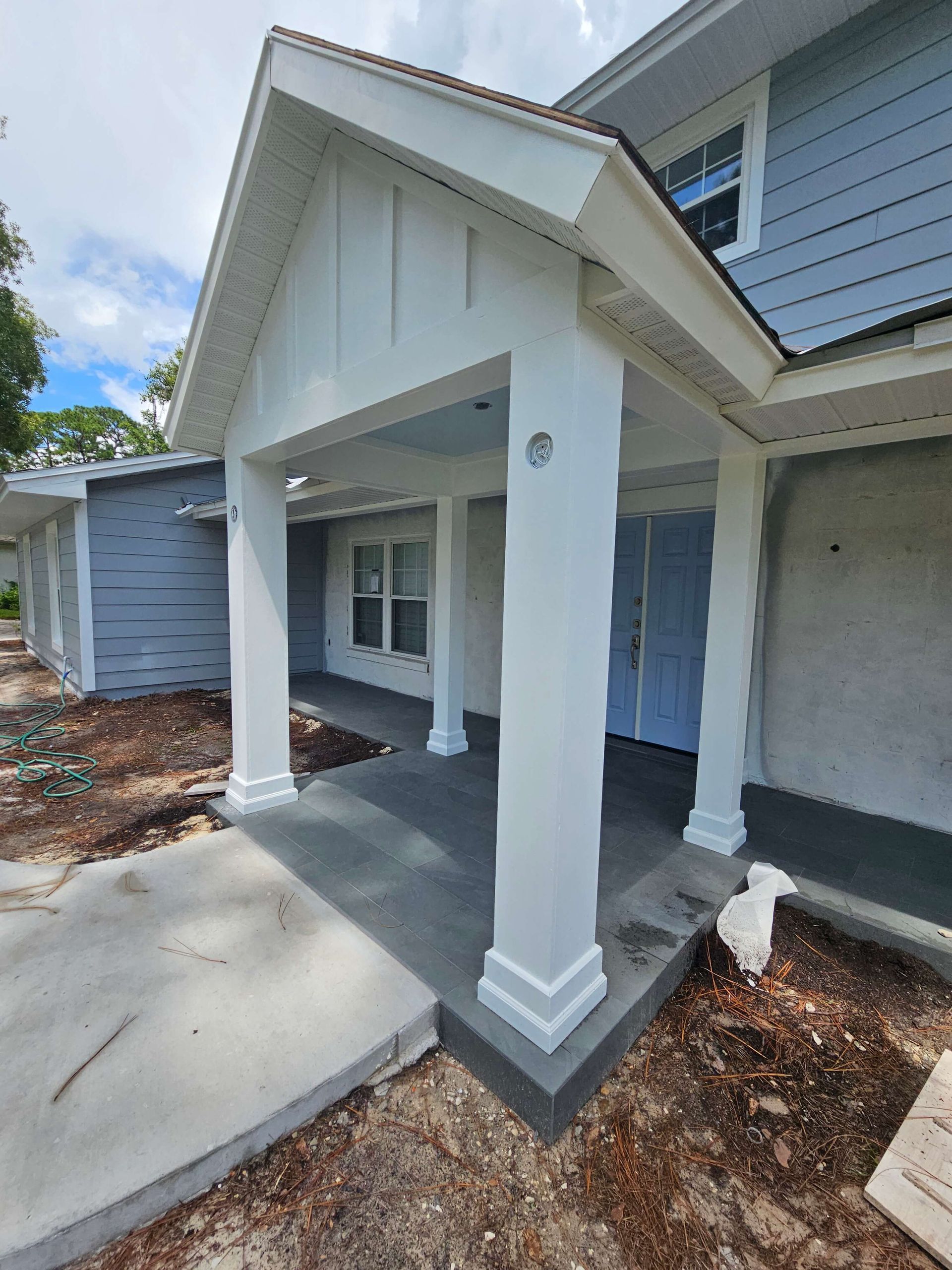 Covered front porch of a white house with columns, windows, and a concrete walkway