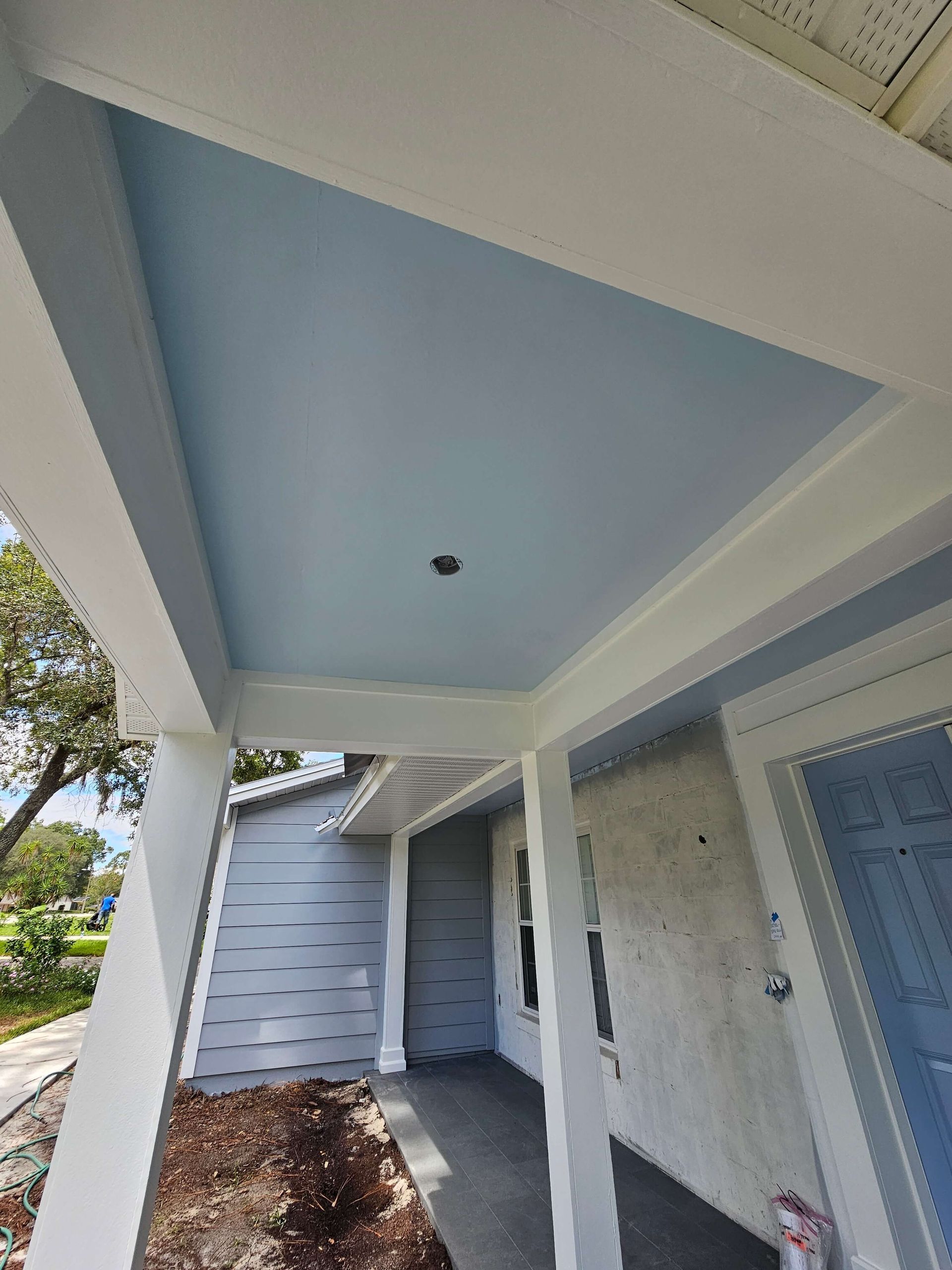 Covered front porch with blue ceiling, white beams, and a blue front door beside a walkway and landscaping.