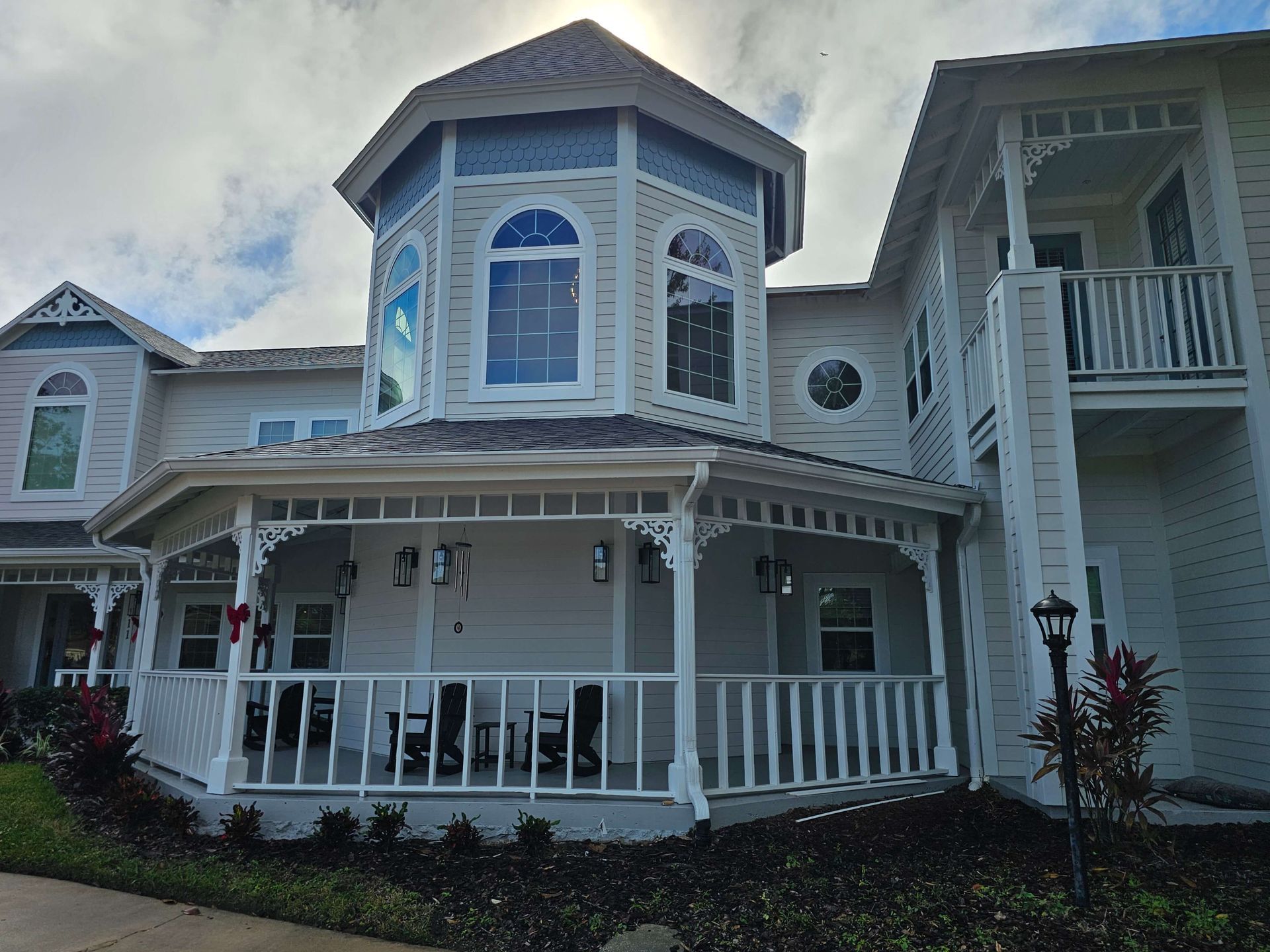 Two-story blue house with white porch and balcony, surrounded by landscaped shrubs.