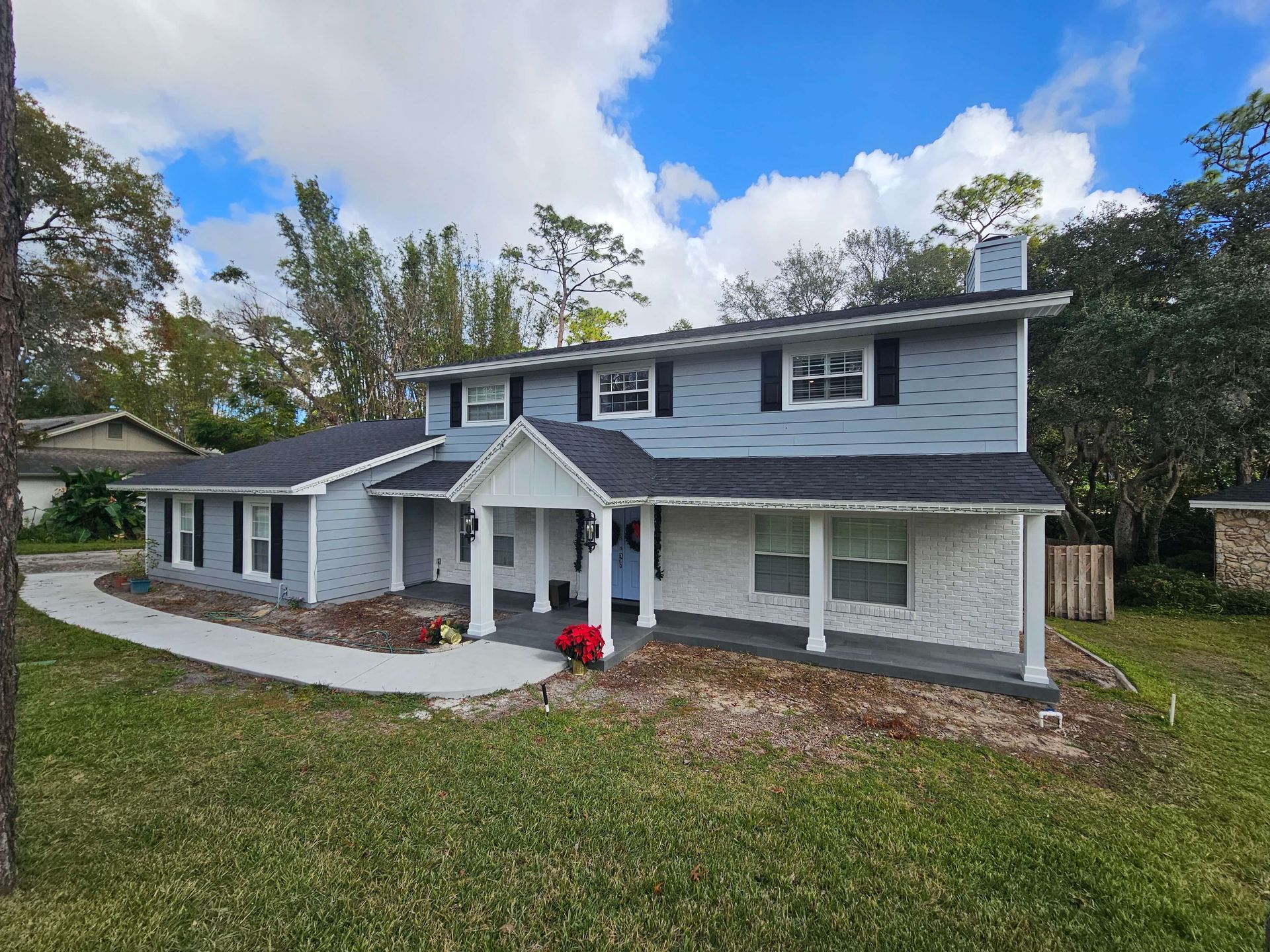 Two-story gray house with white trim, front porch, and curved walkway in a leafy yard