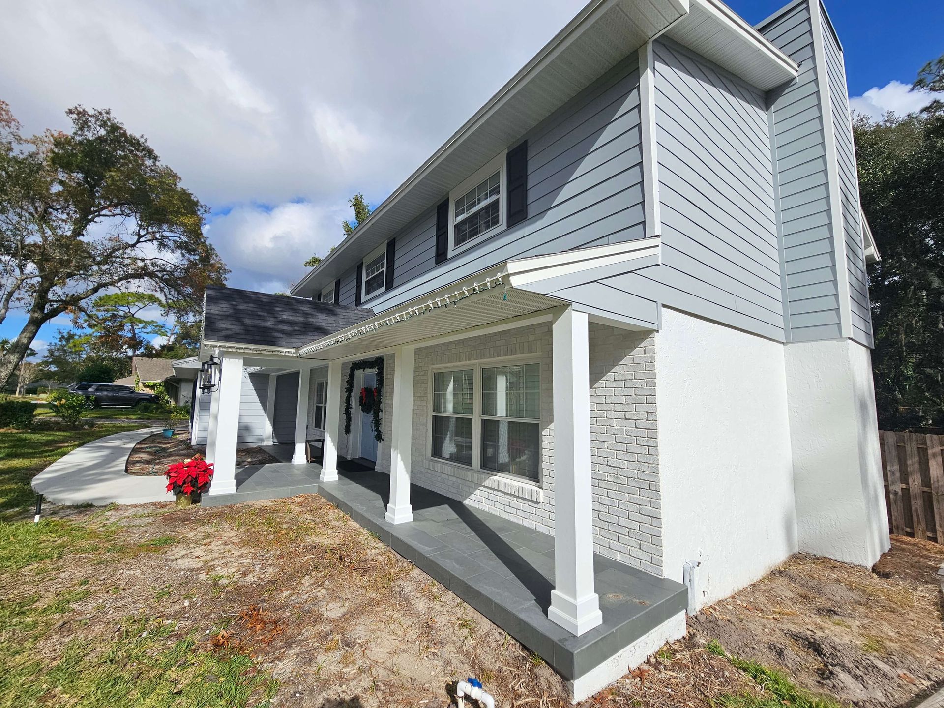 Two-story gray house with white porch and columns, viewed from the front yard on a sunny day