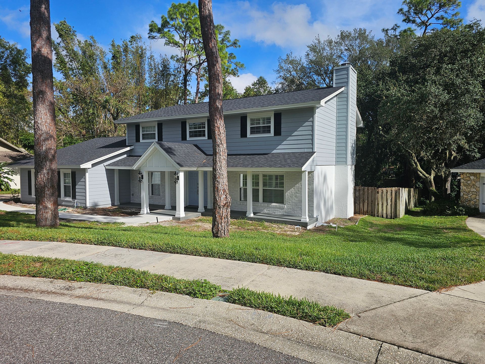 Two-story gray house with white trim, a front porch, and a curved sidewalk under a blue sky