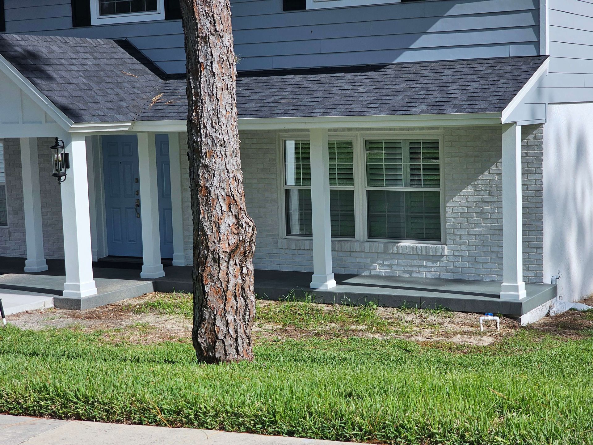 Suburban house porch with white columns, gray siding, and a tree in the front yard