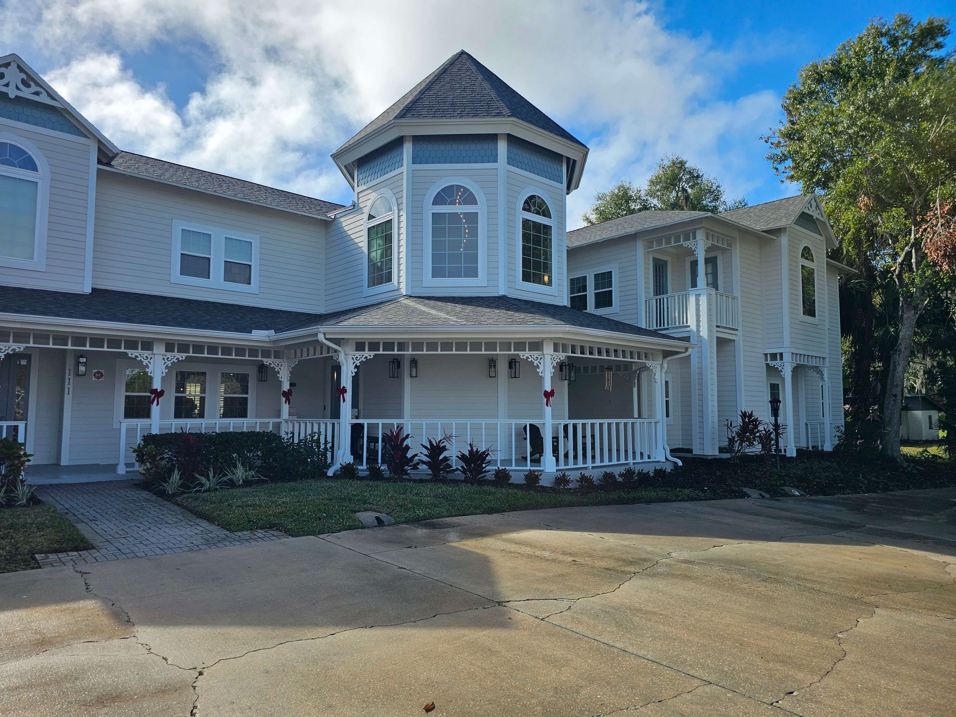 Large white coastal-style house with wraparound porch and turret under a blue sky