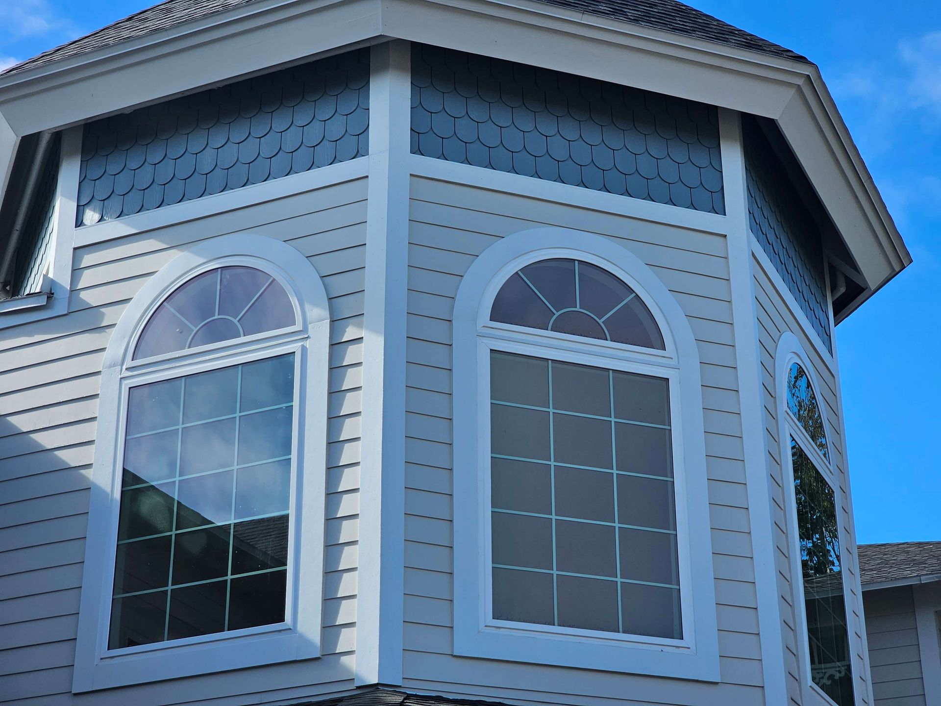 Close-up of a house exterior with white siding, blue trim, and three arched windows under an octagonal roofline