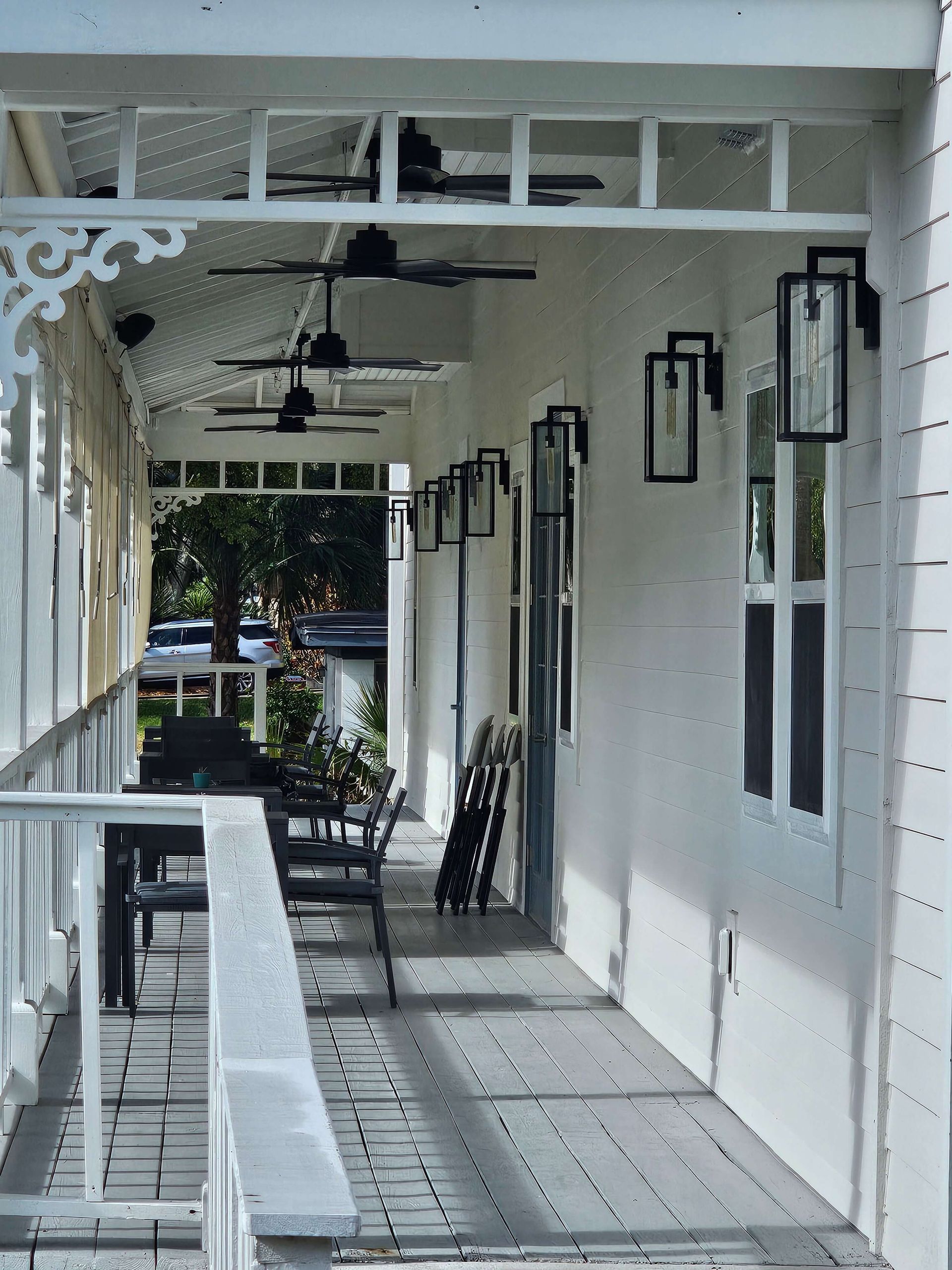 White porch walkway with hanging lanterns, ceiling fans, and benches outside a building