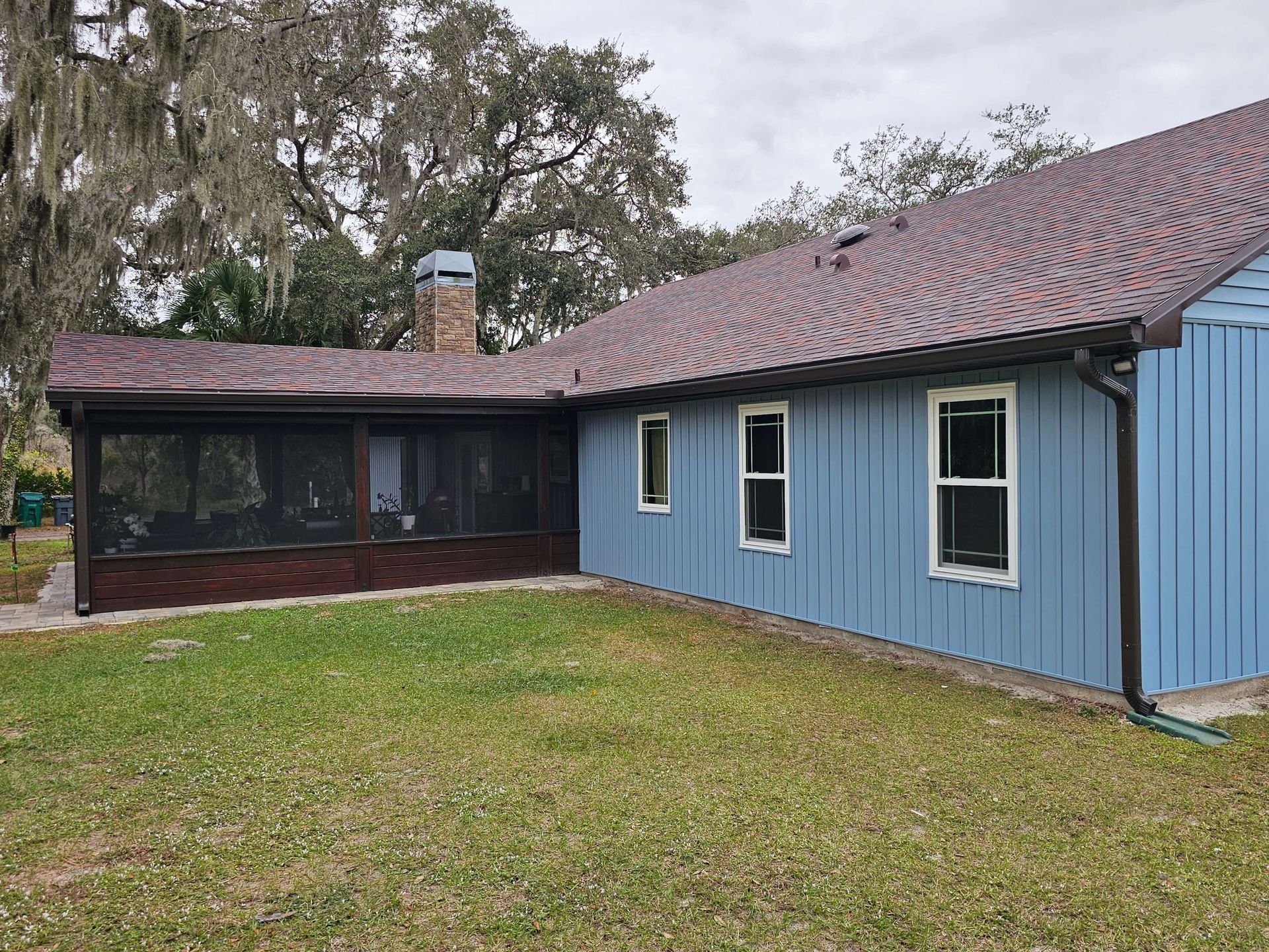 Blue house with screened porch, brick foundation, and a grassy yard under cloudy skies