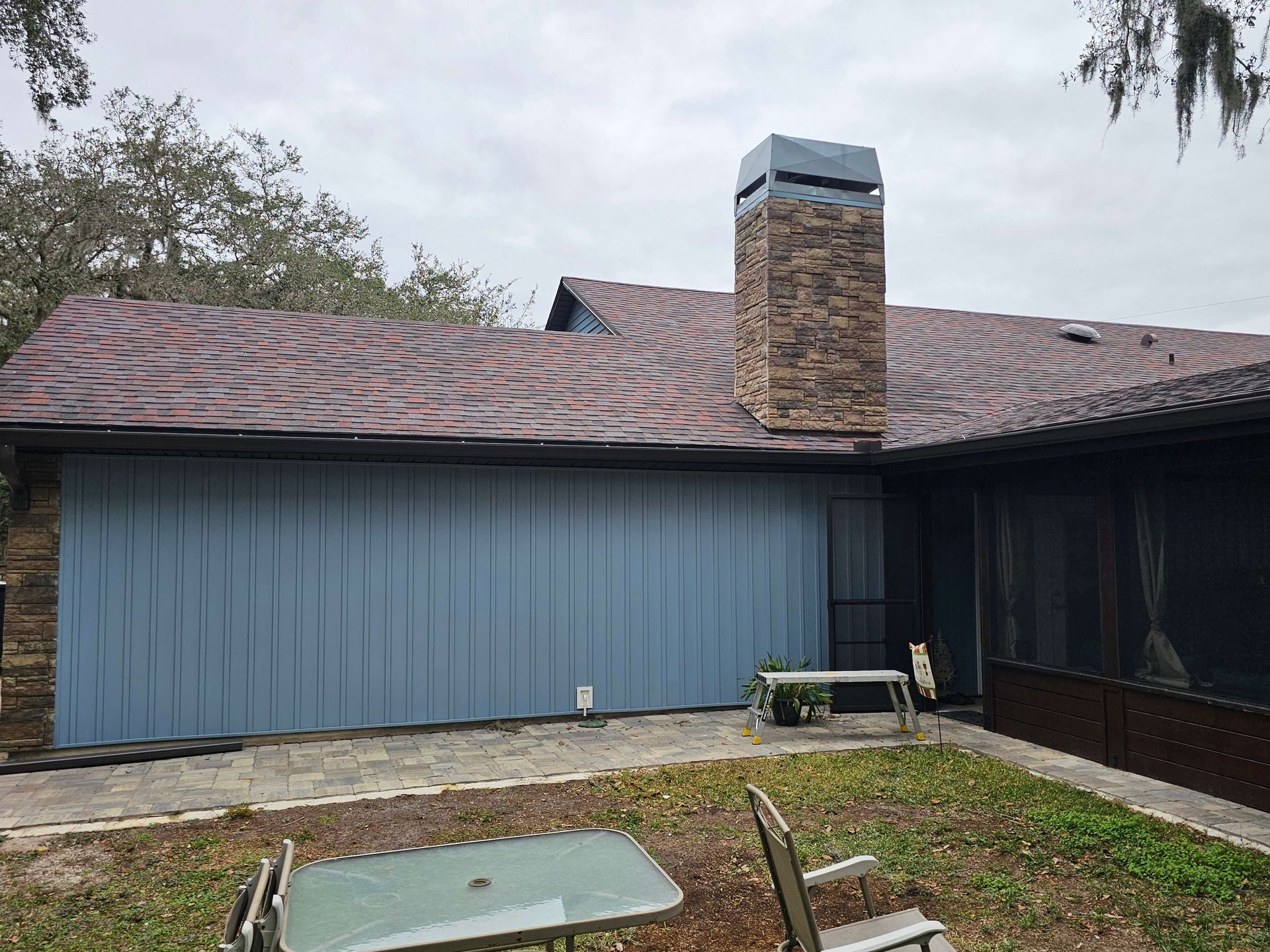 Single-story house with blue siding, shingled roof, central brick chimney, and small yard in front