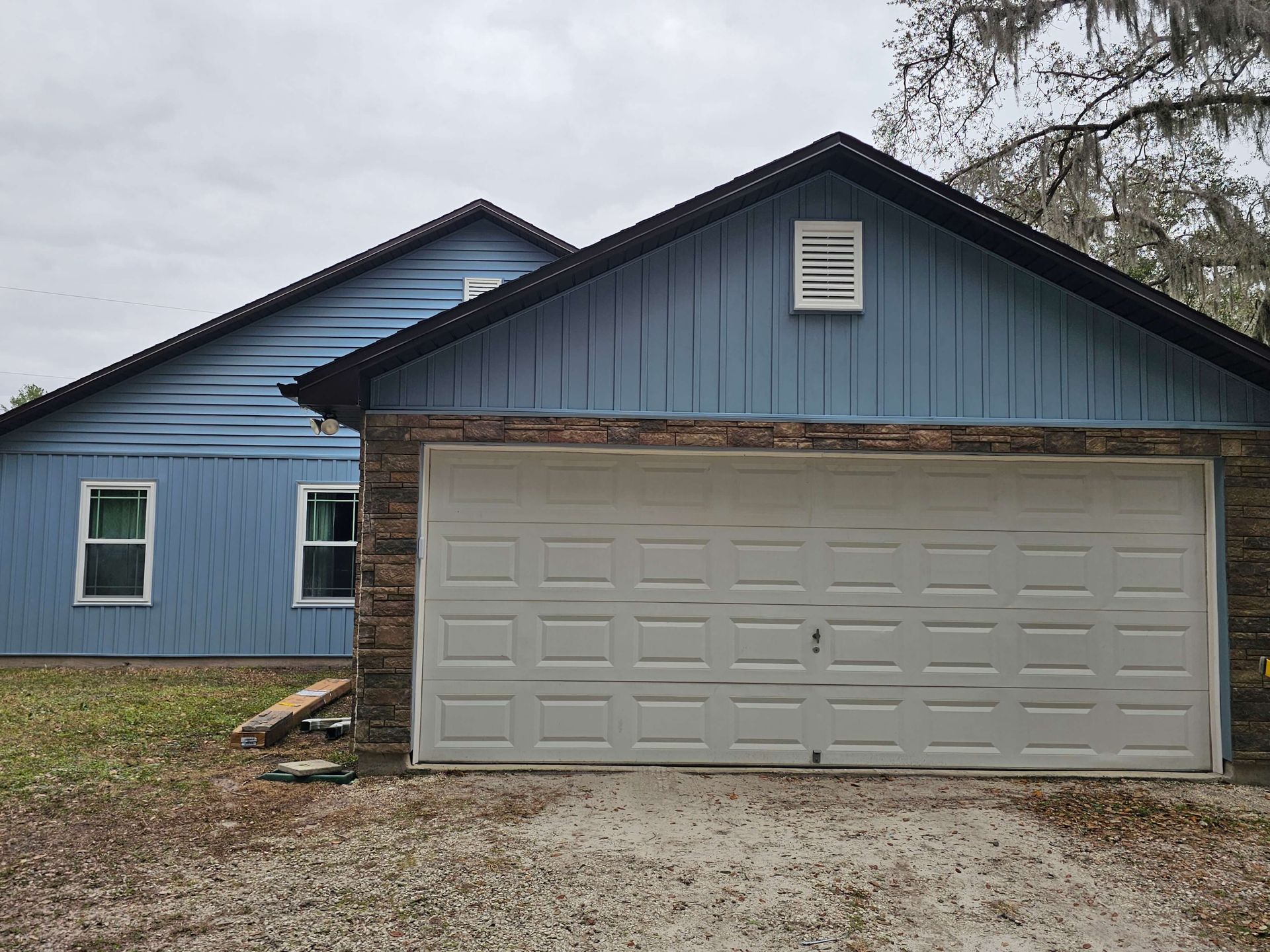 Blue house with a beige garage door and dark roof under overcast sky