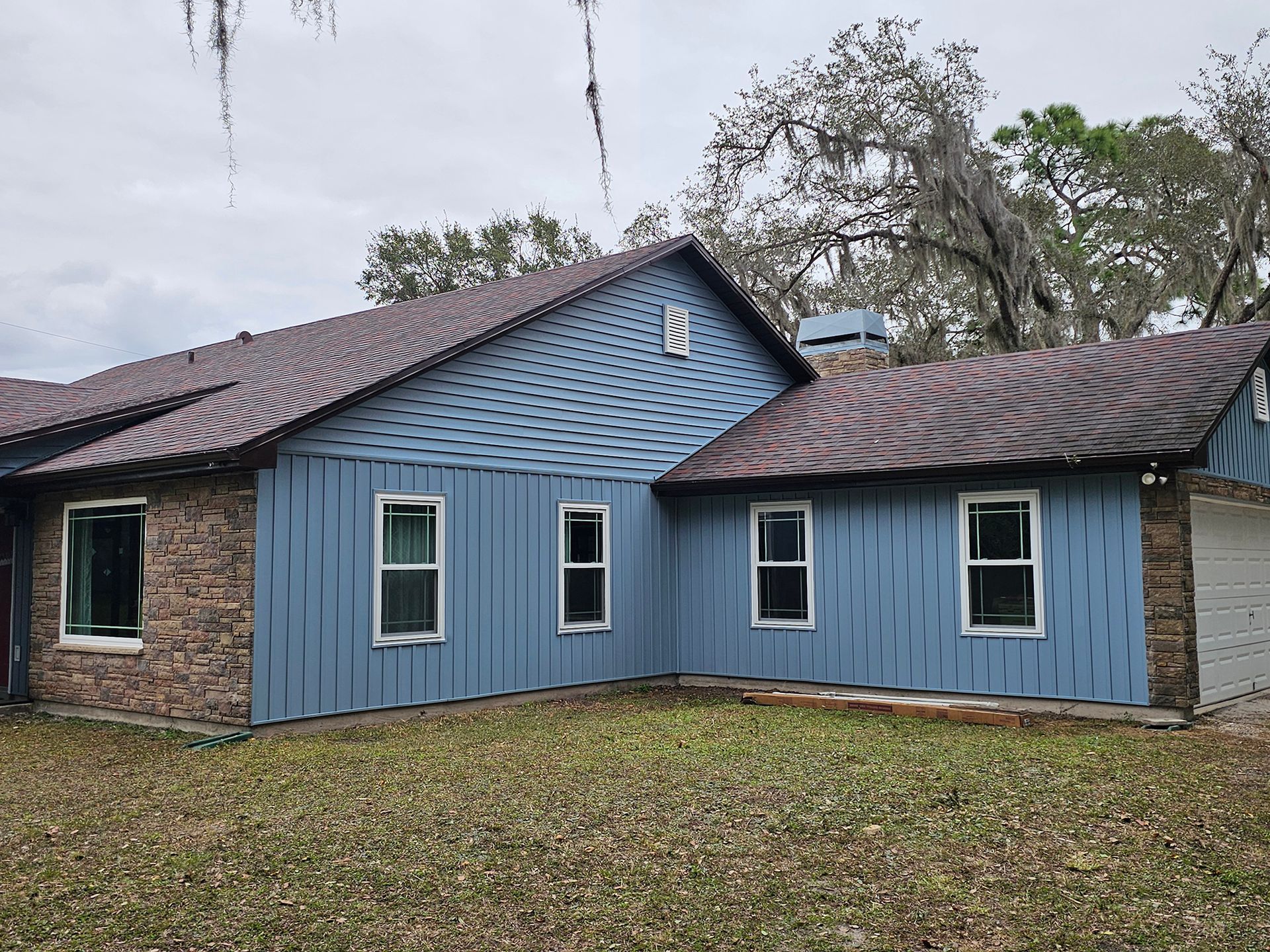 Blue house with brick side wall and dark shingle roof on a grassy lot