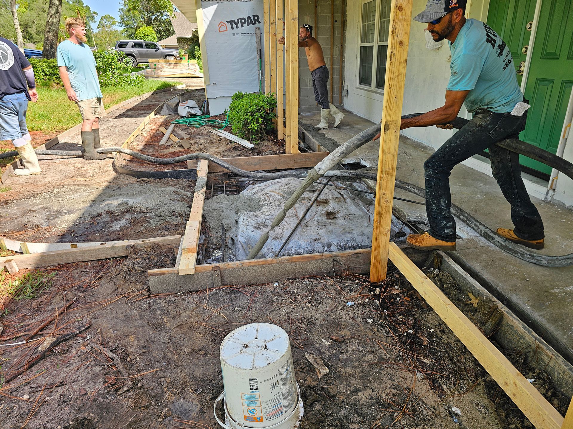 Workers pour wet concrete into a wooden foundation form on a construction site.