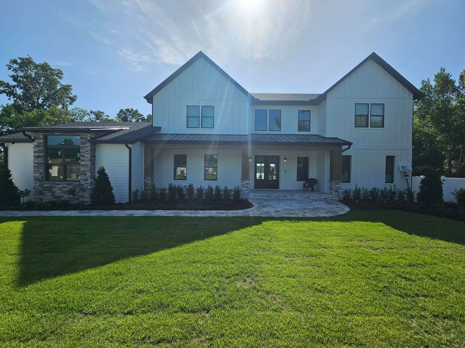 Sunlit two-story white house with a large green lawn and front porch