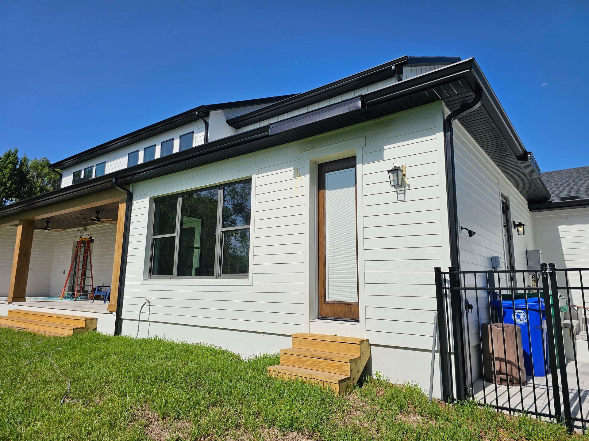 Modern white house exterior with black trim, large windows, porch, and front steps under a blue sky