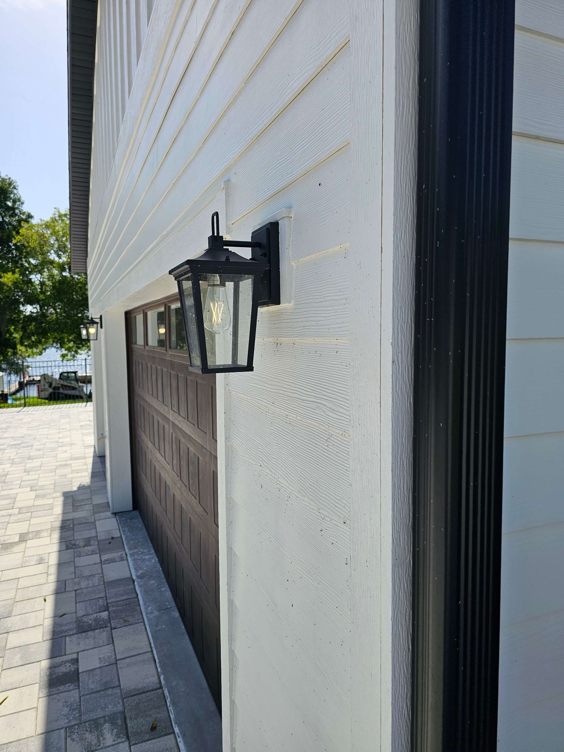 Black lantern wall light on a white stucco building beside a garage door and sidewalk