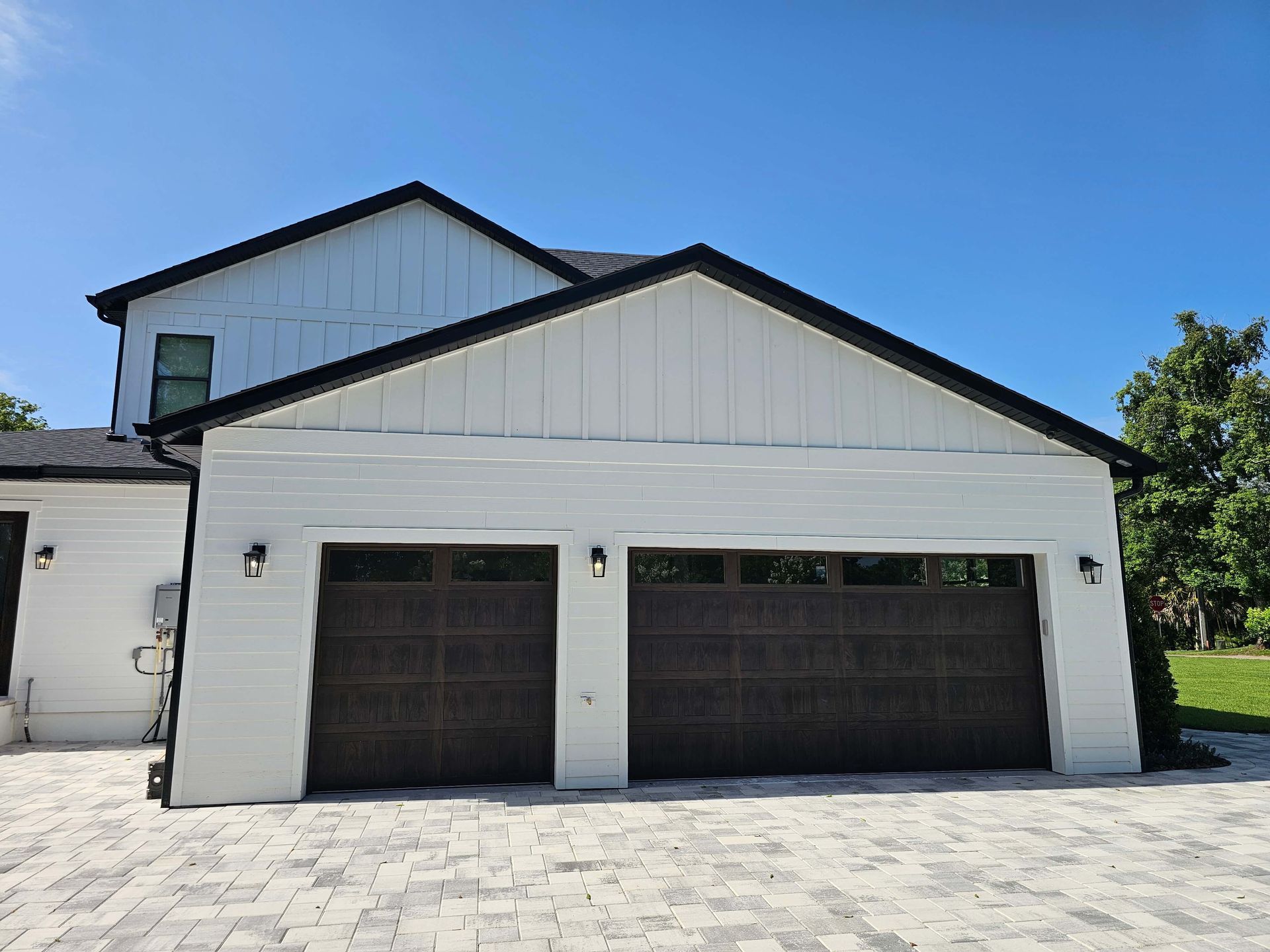 White two-story house with a black double garage and paved driveway under a blue sky
