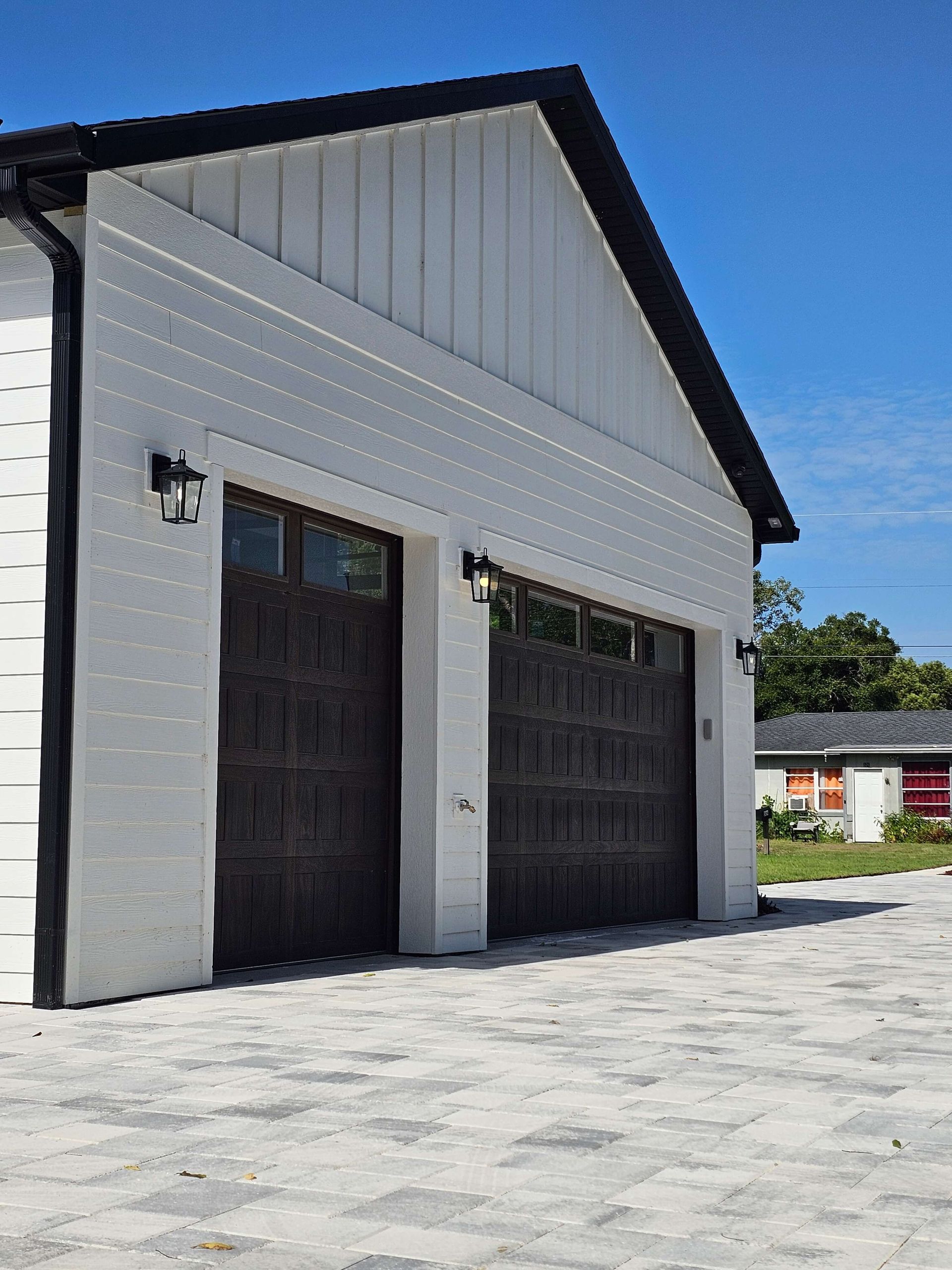 White garage with two dark doors and black trim under a blue sky, viewed from the driveway