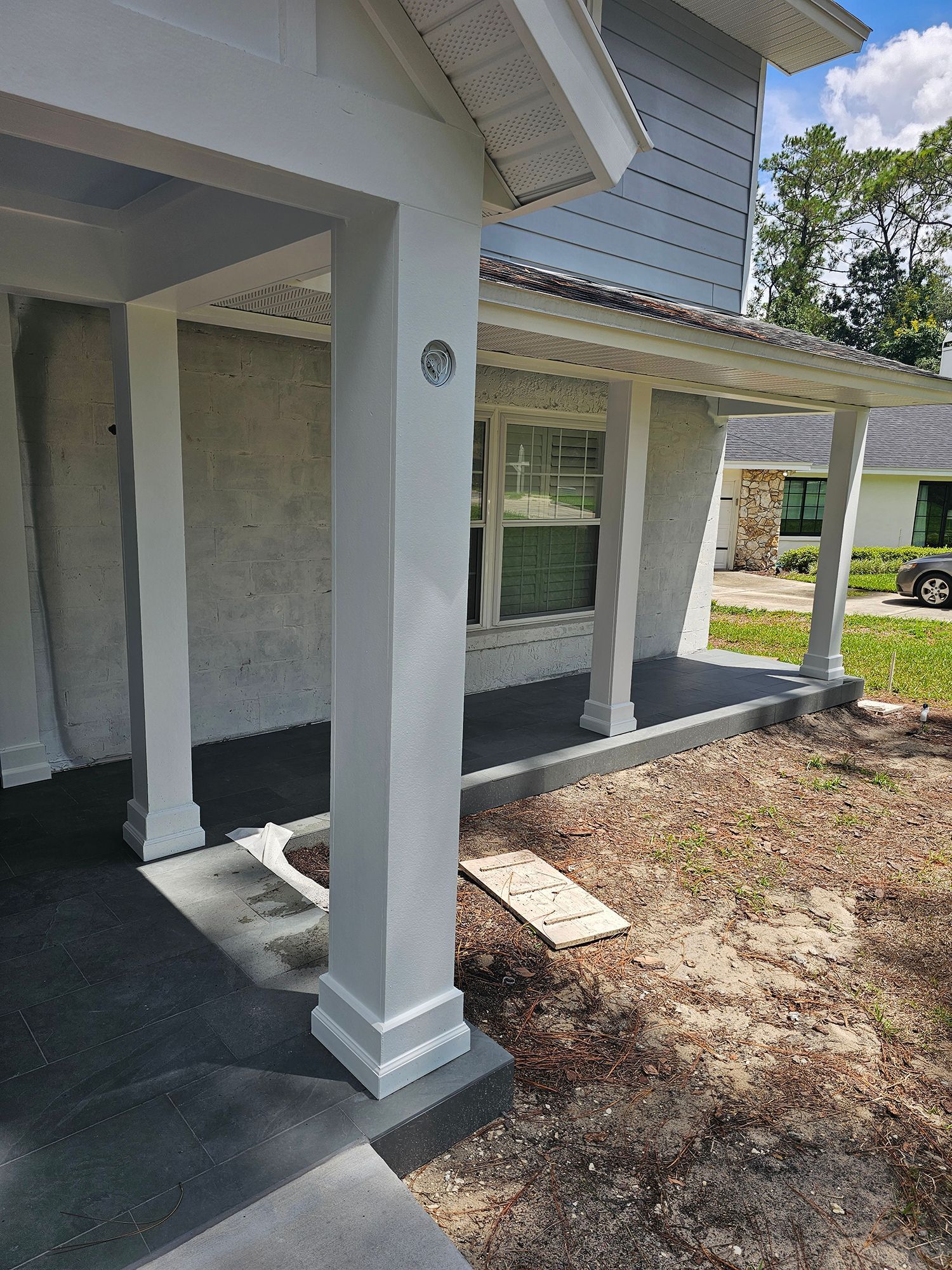 Front porch of a house with white columns, gray siding, and a concrete walkway beside a patchy yard.