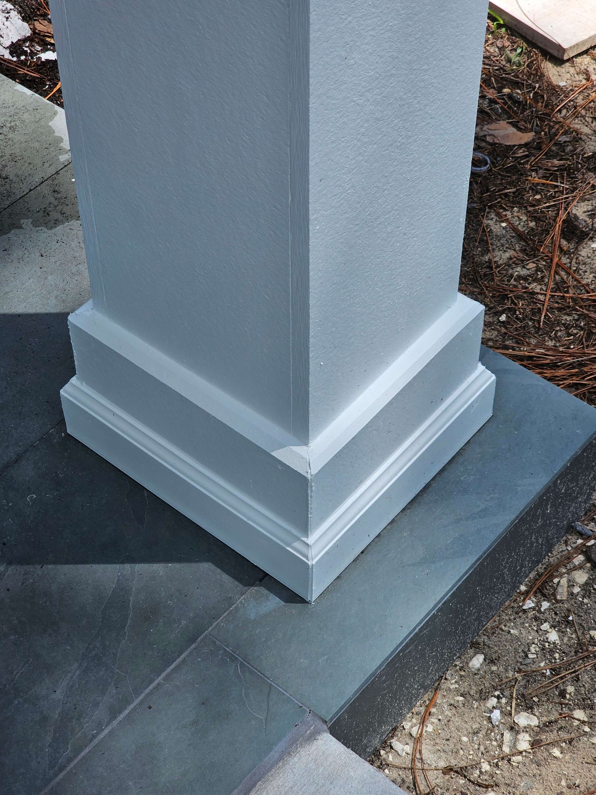 Gray pillar base on a stone patio corner, with dark pavers and gravel nearby.
