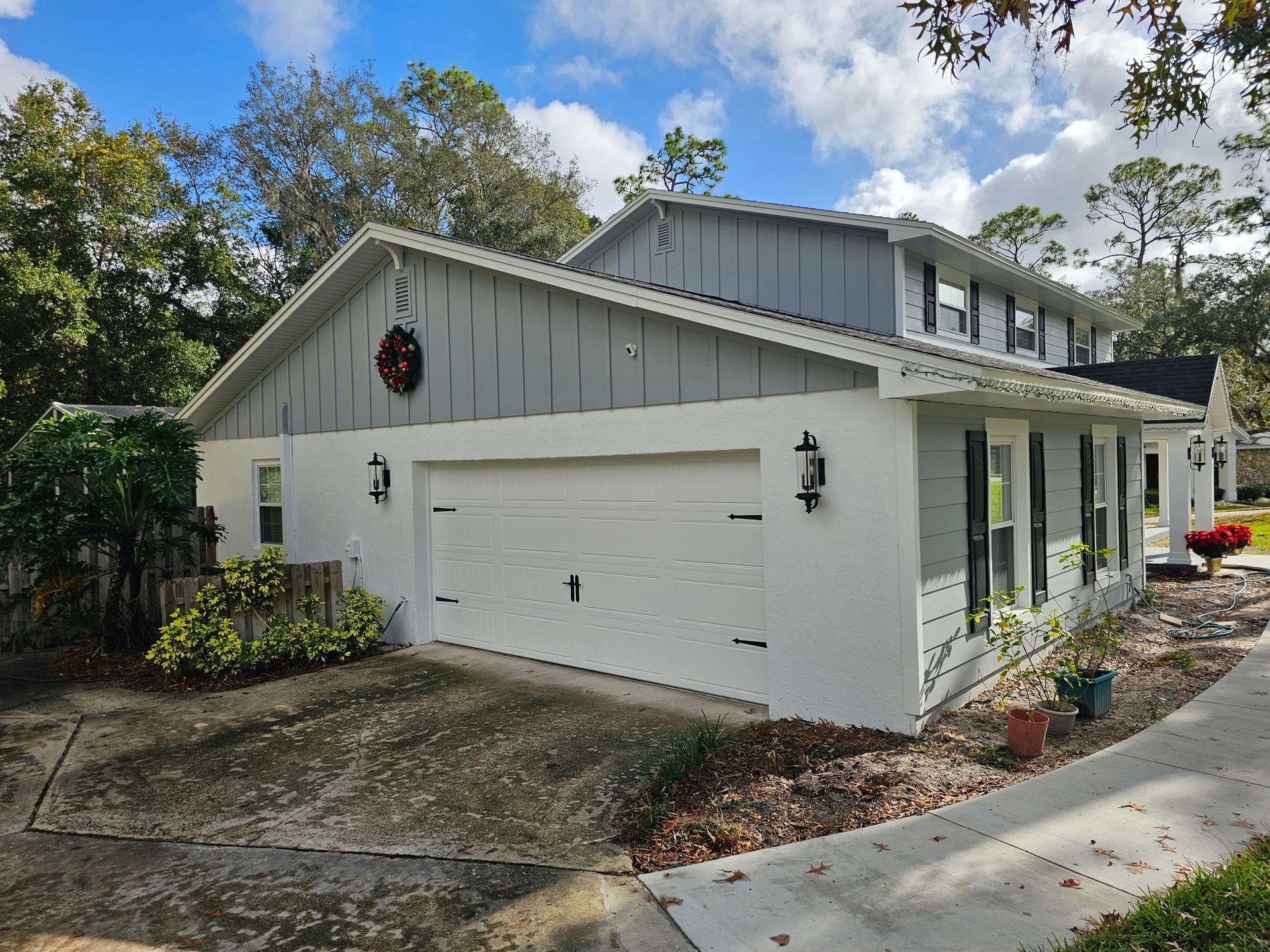 White two-story house with a double garage, black sconces, and a curved driveway under a partly cloudy sky