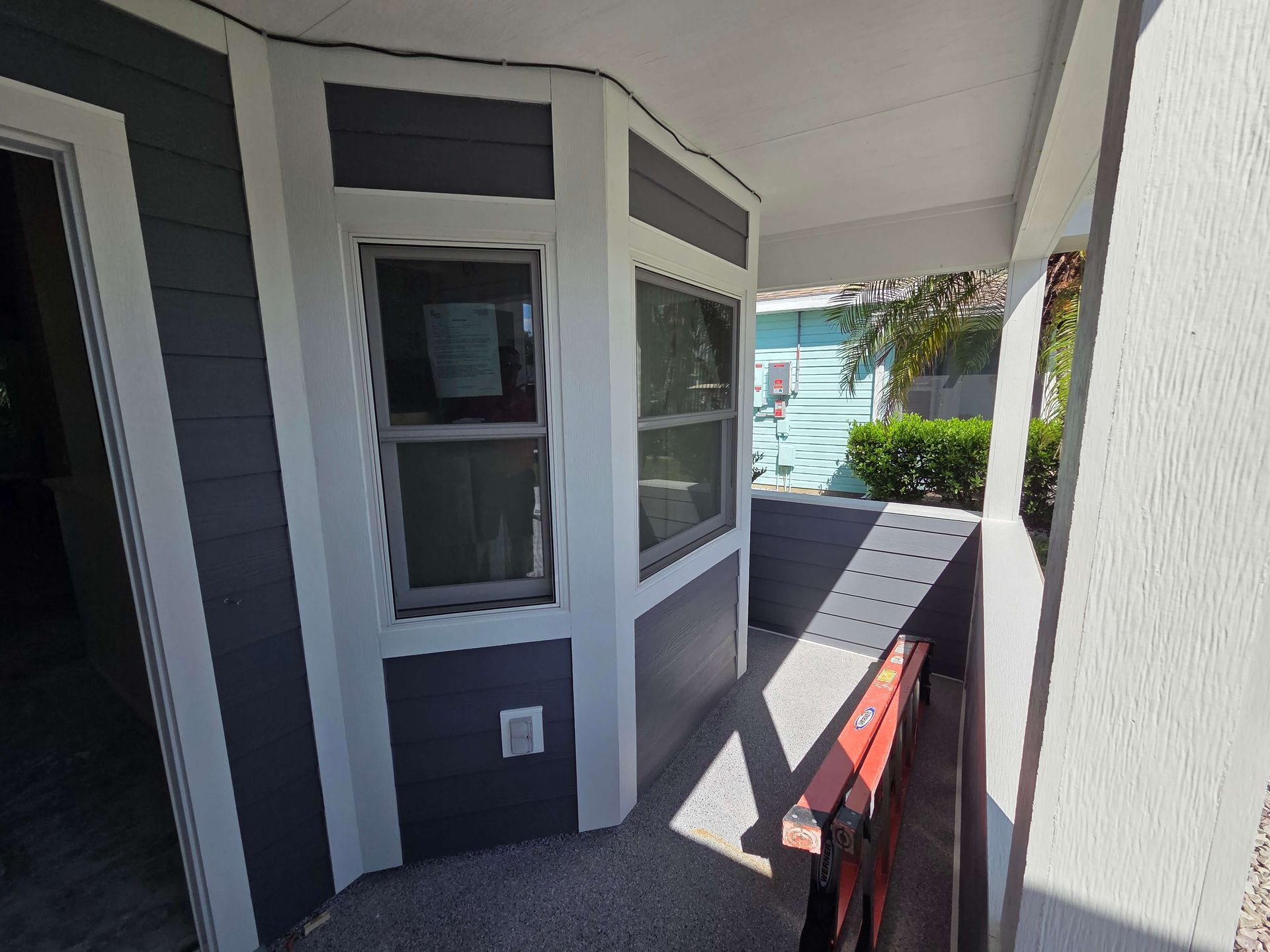 Apartment walkway with gray siding, windows, and a red railing in sunlight