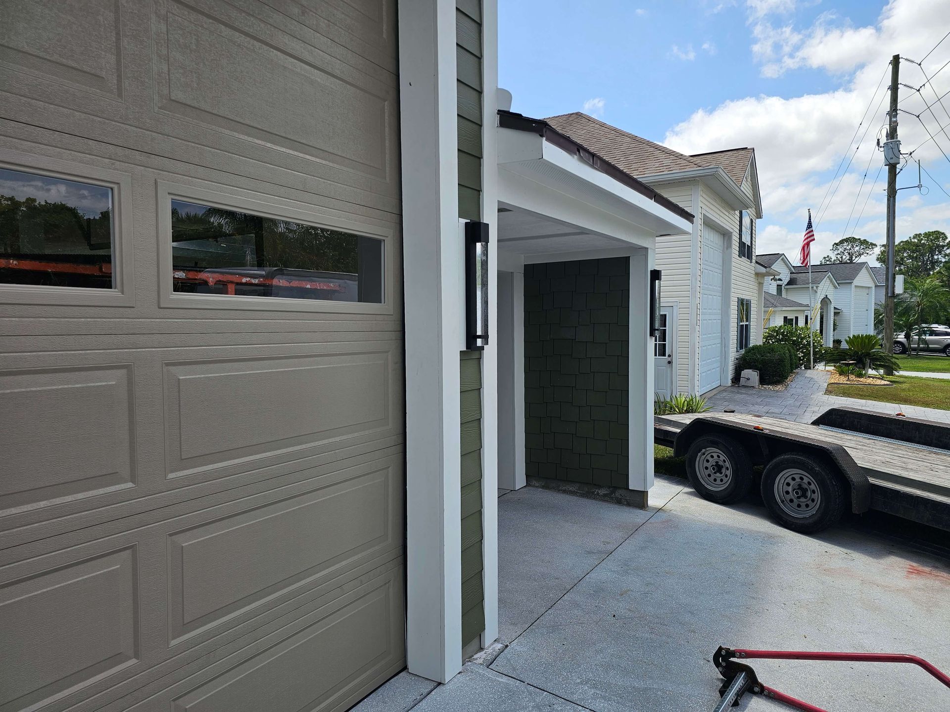 Garage entrance beside a flatbed trailer, with a partially open door and gray siding.