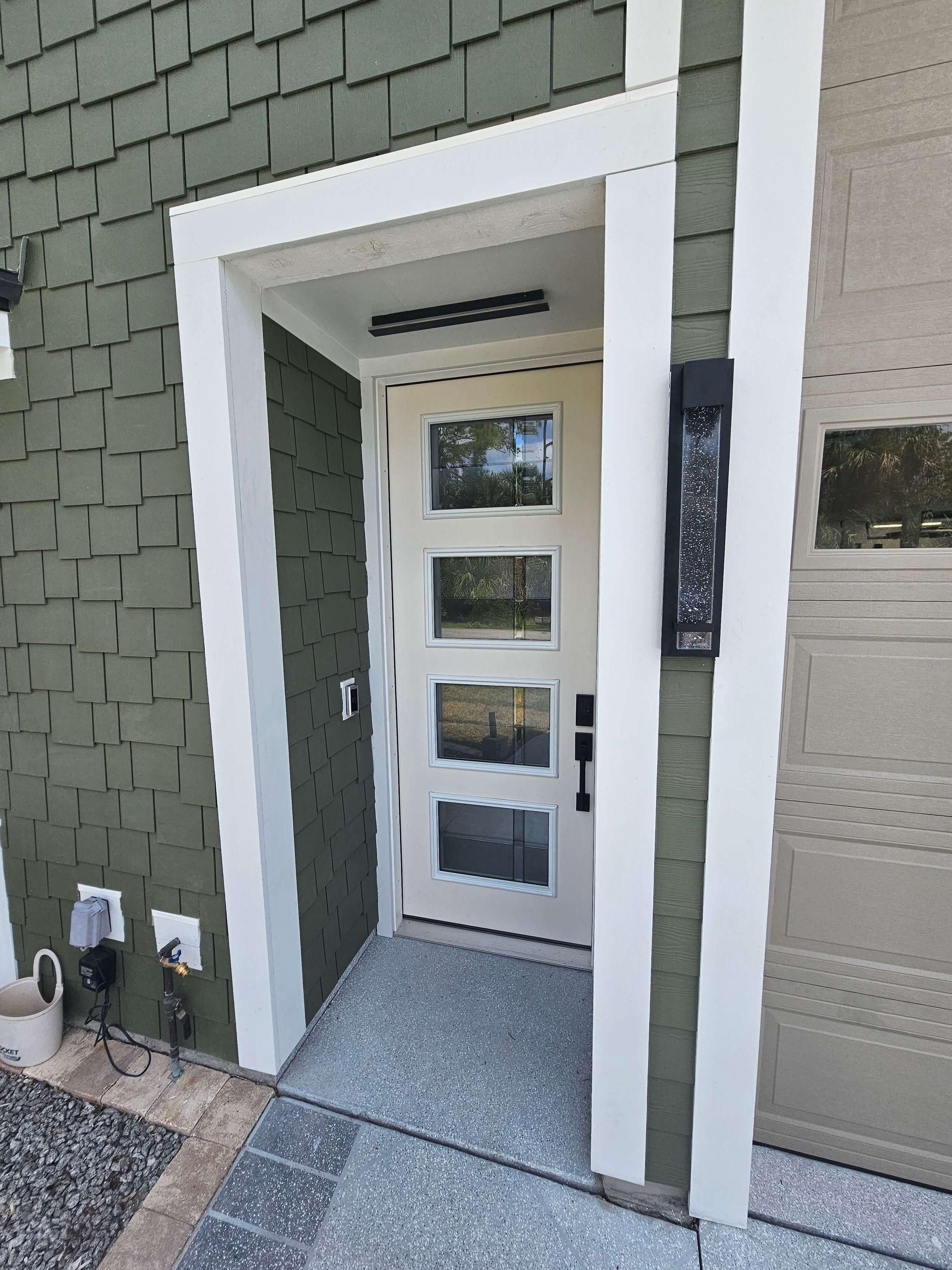 Front entryway with white-trimmed glass door and green siding beside a beige garage.
