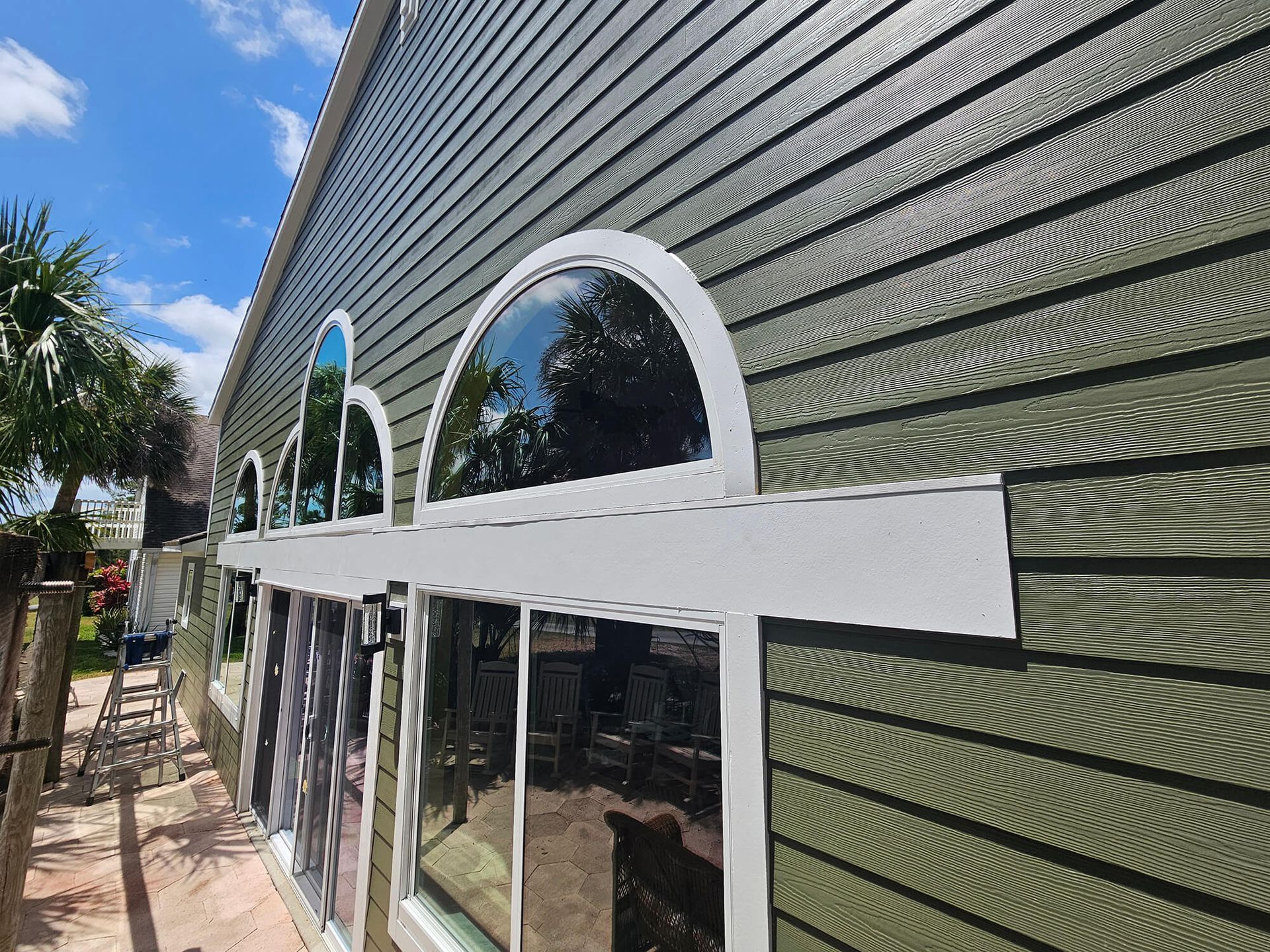 Exterior of a green house with white-trimmed arched windows and a covered walkway
