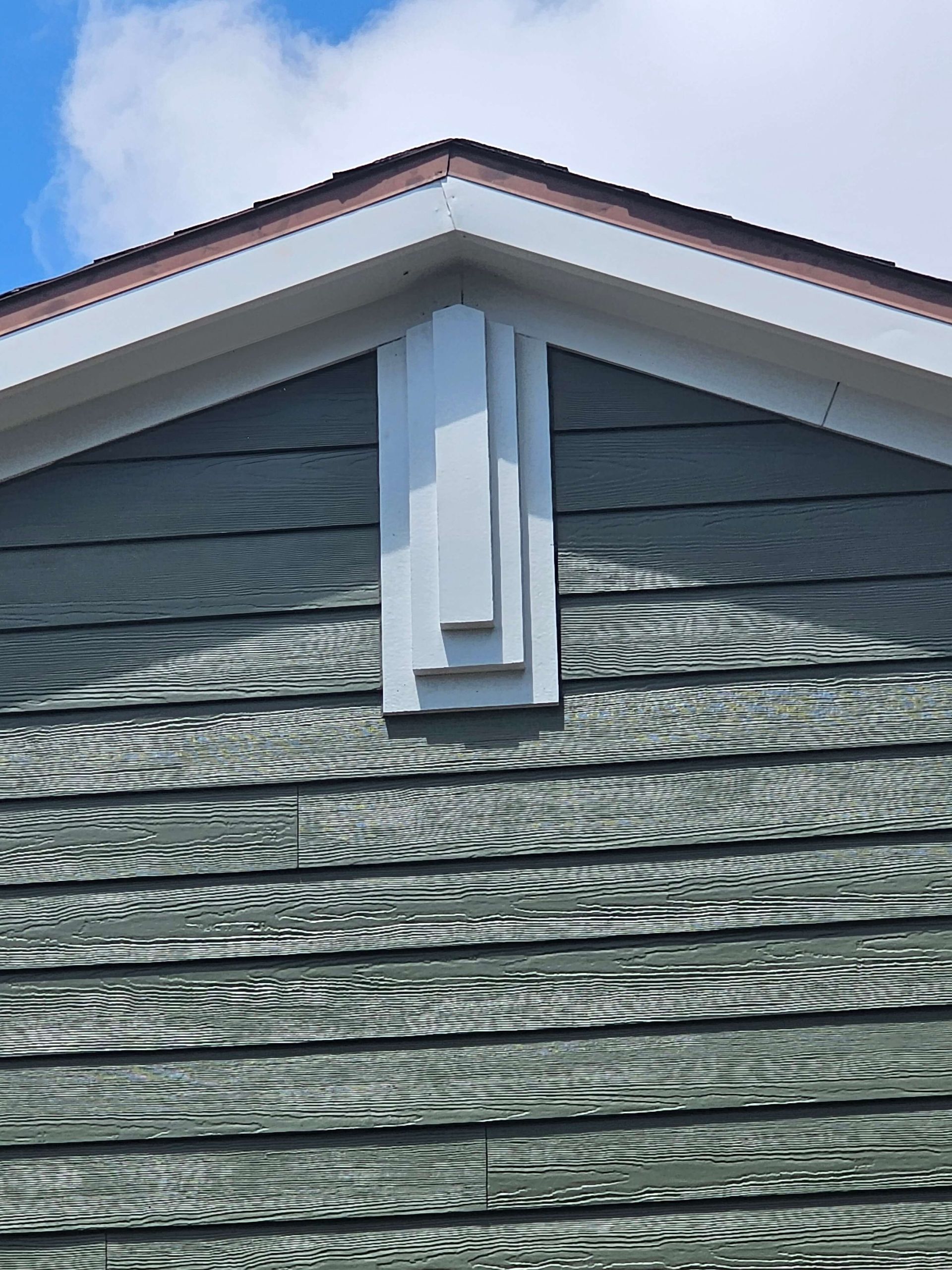 House gable with gray siding and white trim, featuring a white decorative bracket under the roof peak