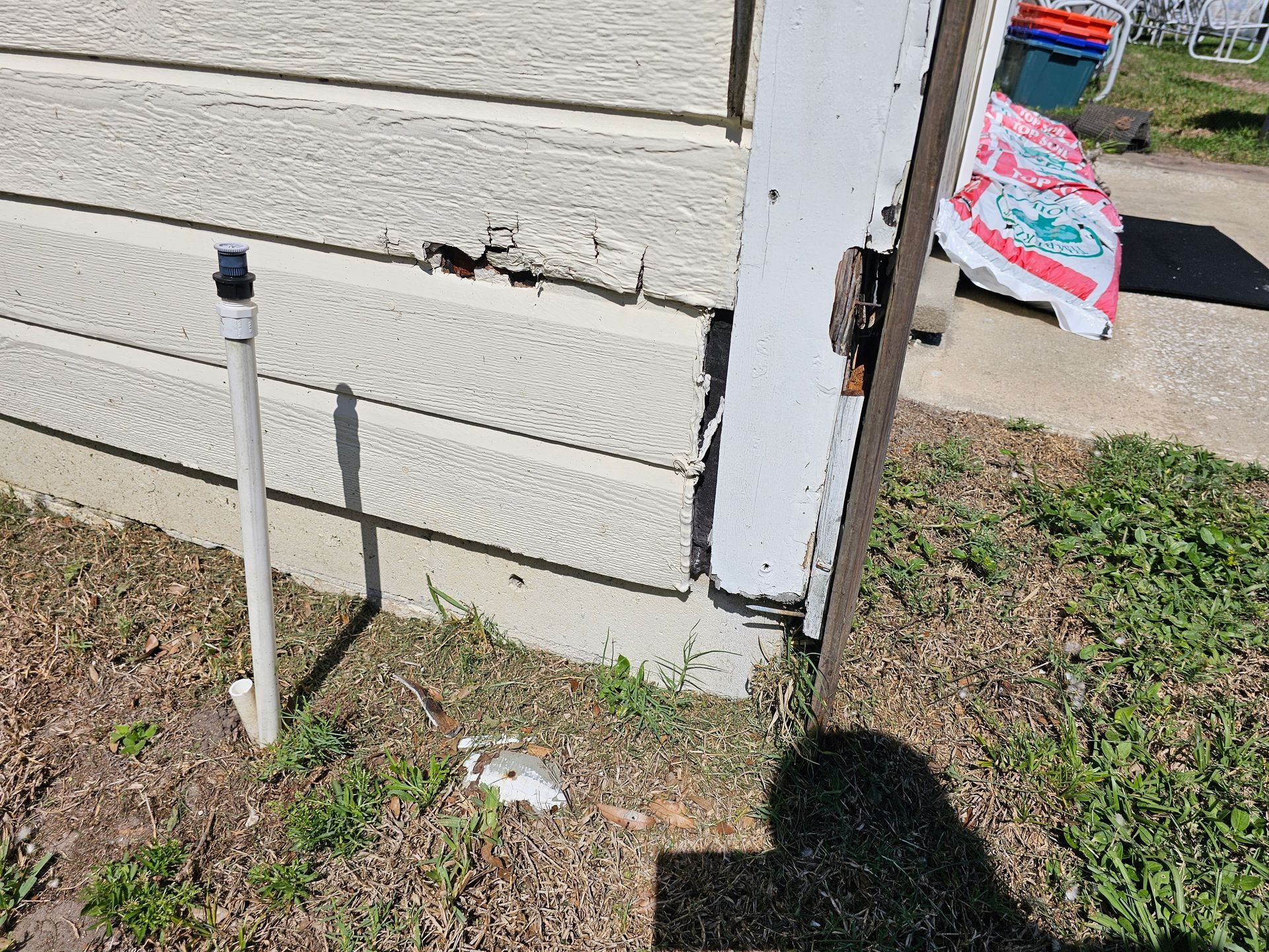White exterior house wall with a capped white PVC pipe and a doorway edge beside a patchy yard.