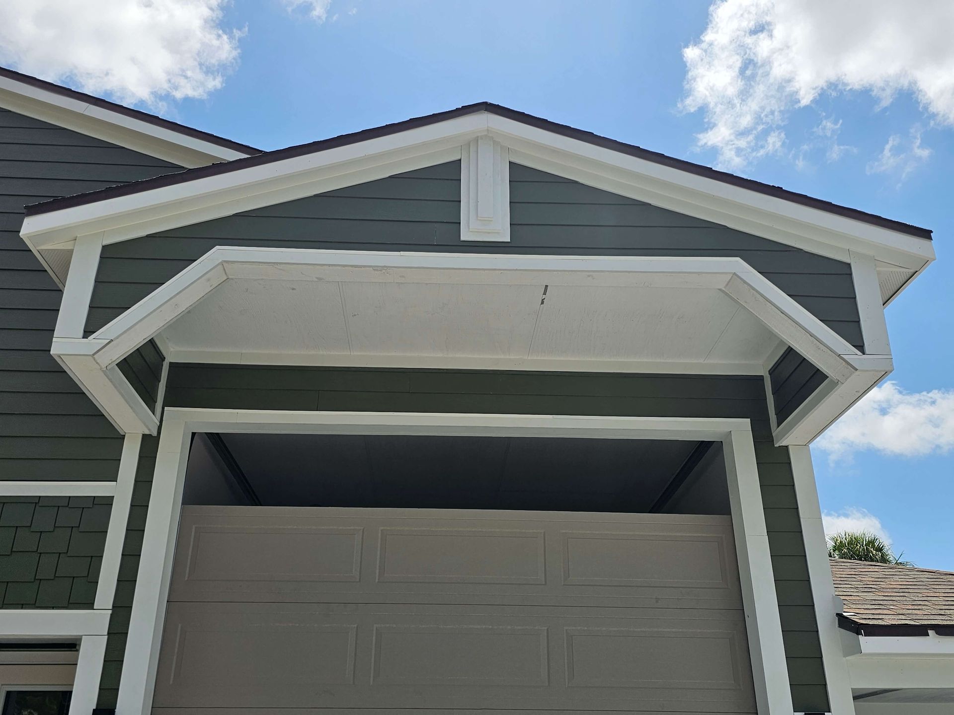 Front view of a house garage with white trim and a light gray door under a blue sky