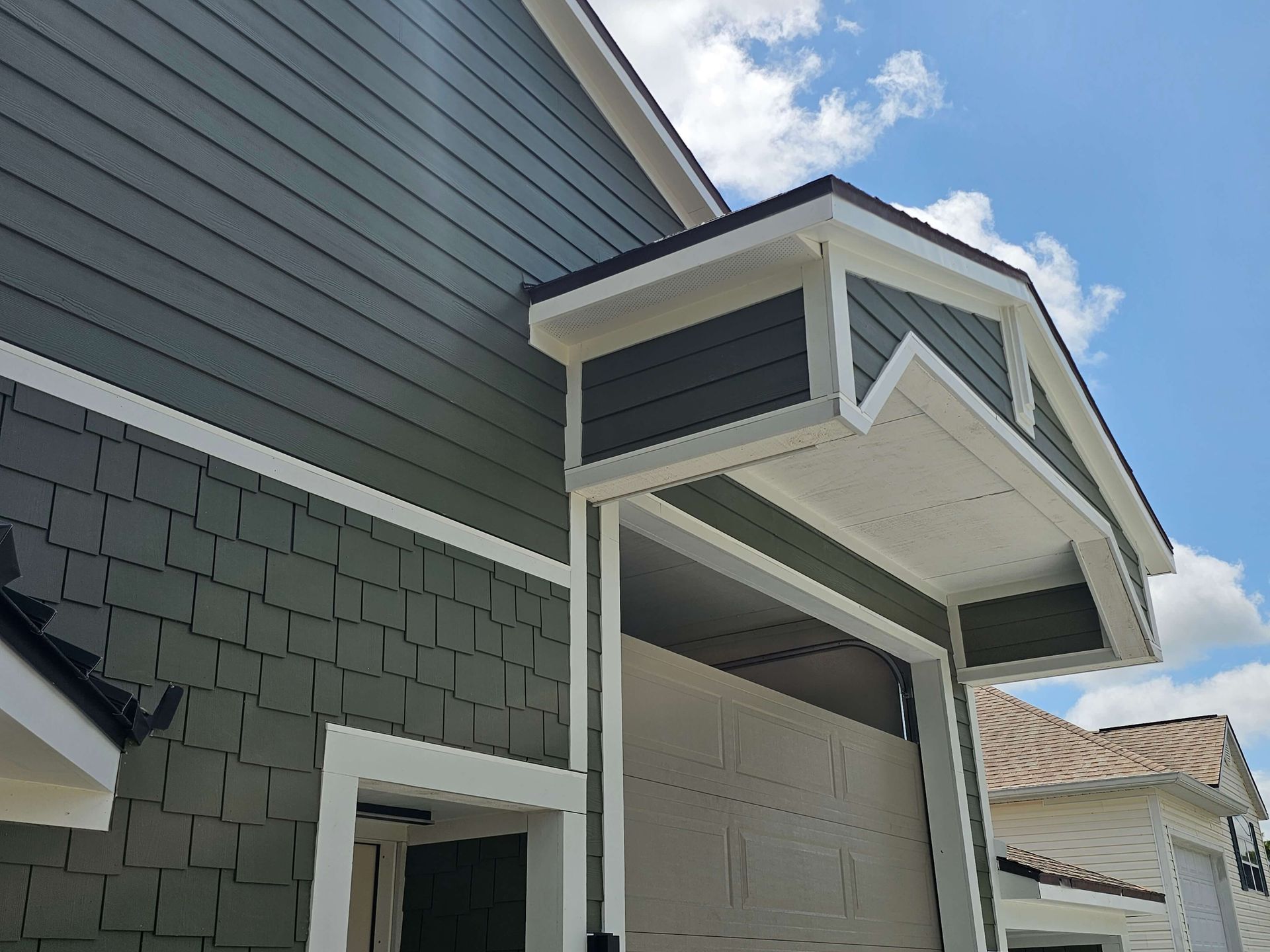 Close-up of a house roof eave and vented dormer with gray siding and white trim against a blue sky