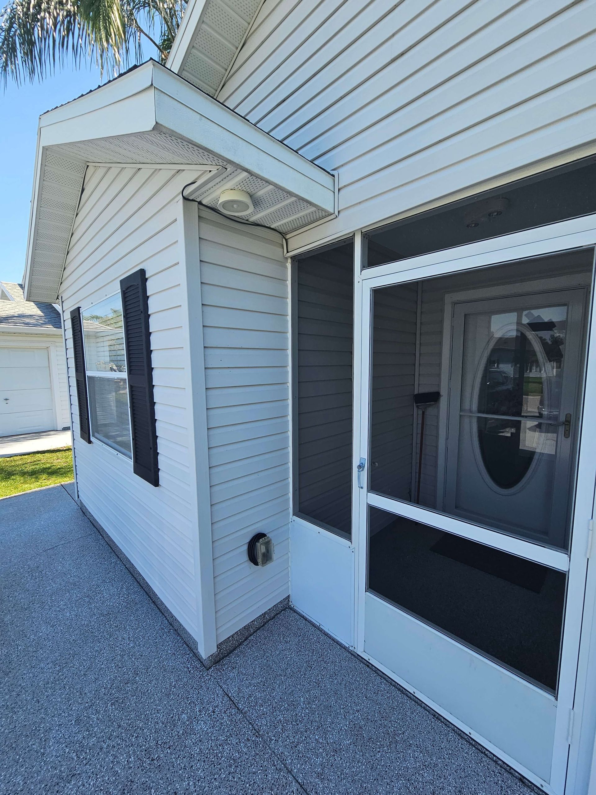 White house exterior with covered entry, black shutters, and a glass storm door over a gravel walkway