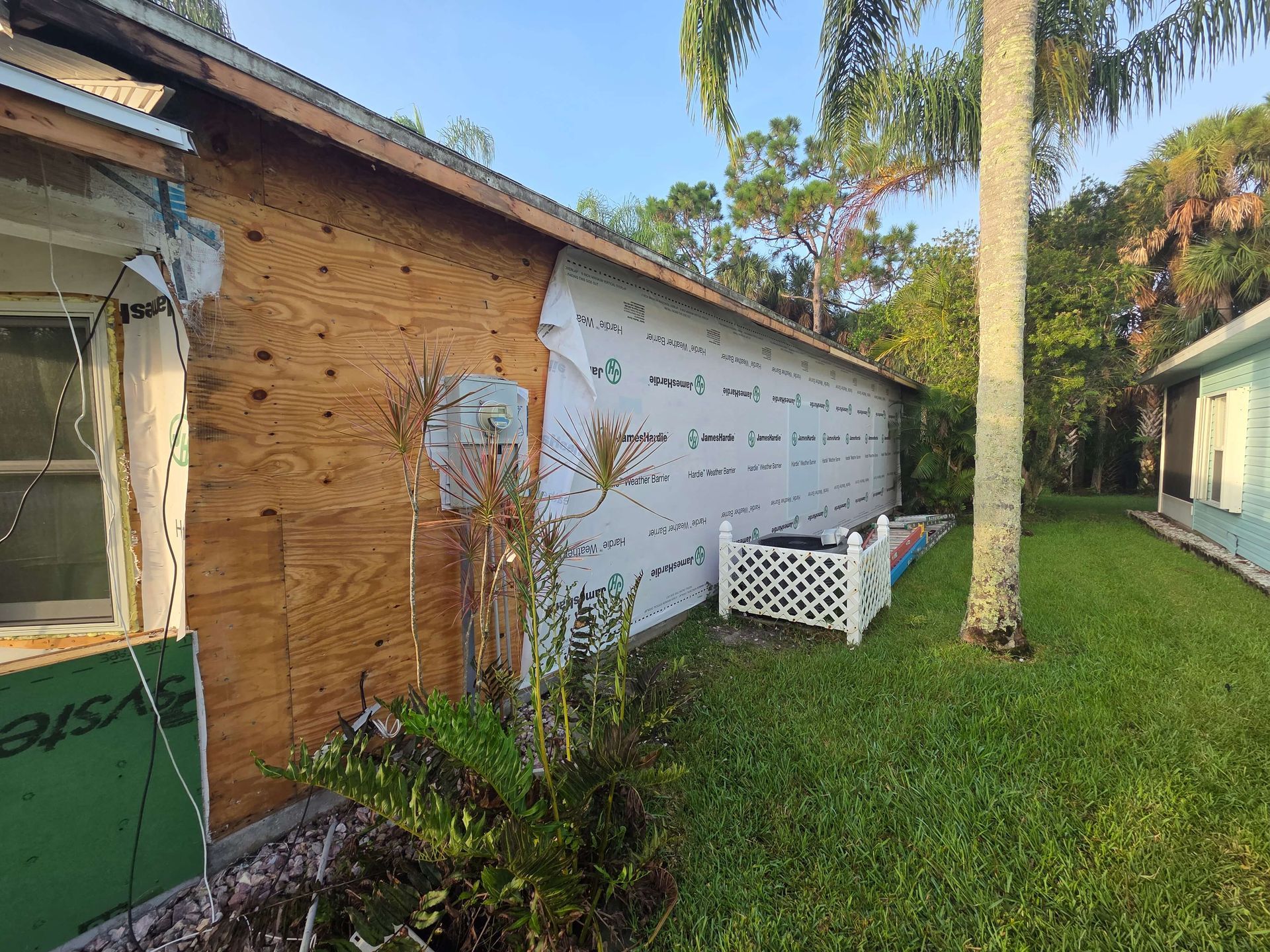 Small brick house side yard with green lawn, tree, and a white lattice structure beside the wall.